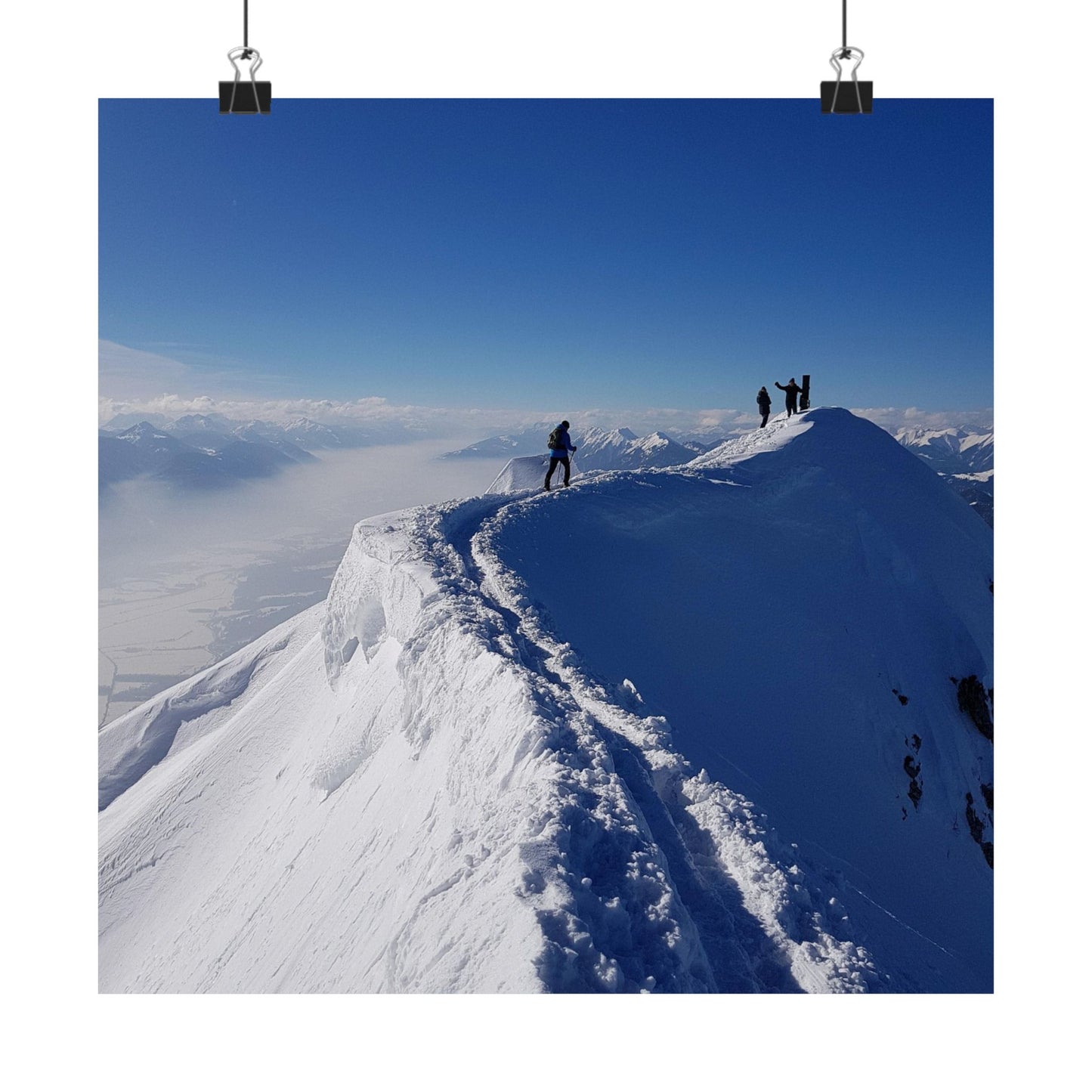 Group of people on a snow-covered mountain ridge with a clear blue sky.