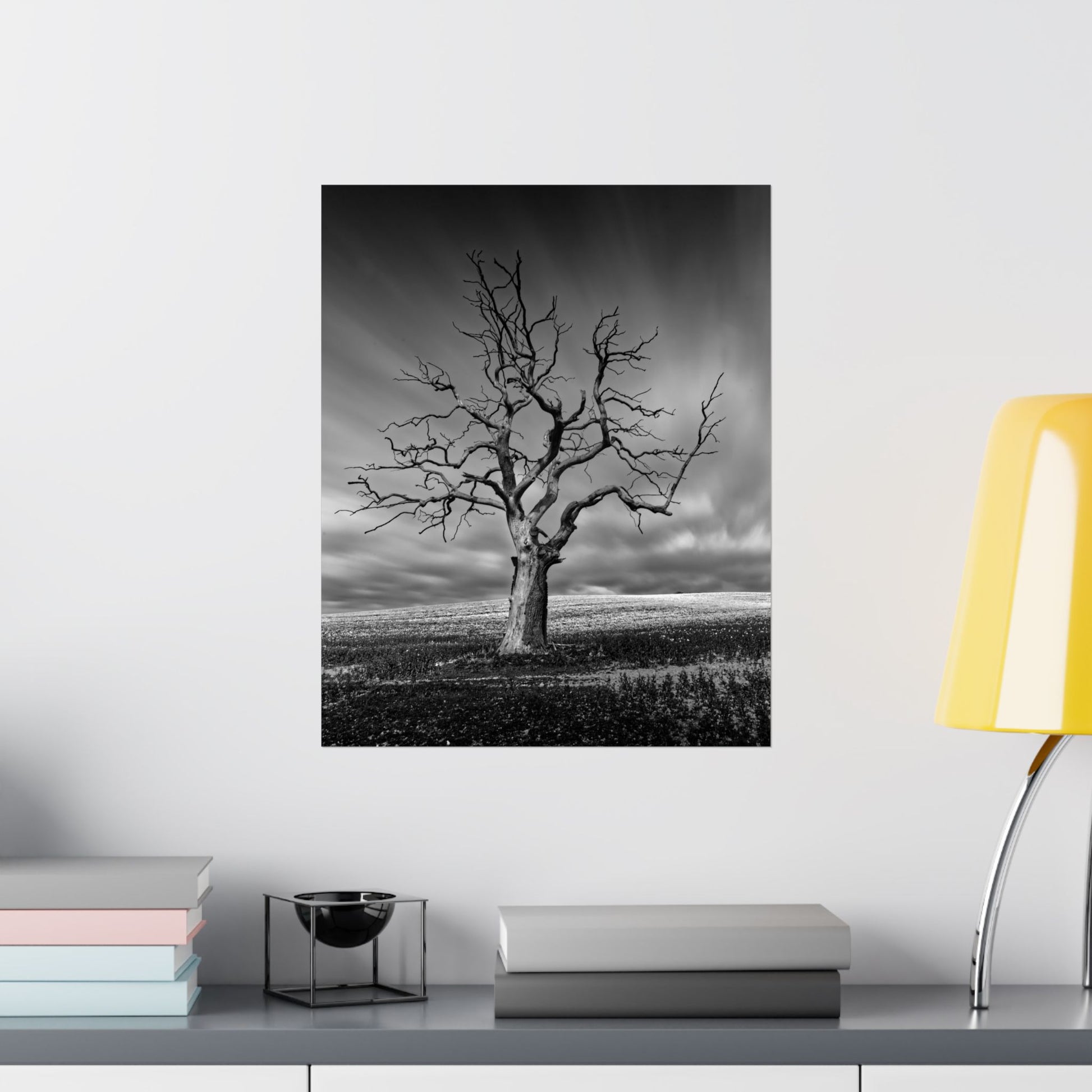 Black and white tree artwork on a wall above a shelf with books and a lamp.