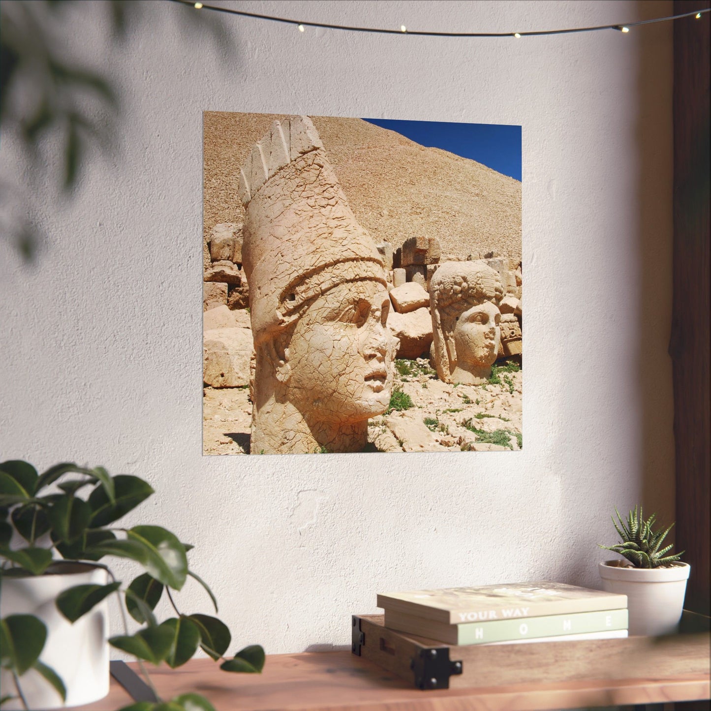 Decorative wall art of stone heads on a white wall with plants and books below.