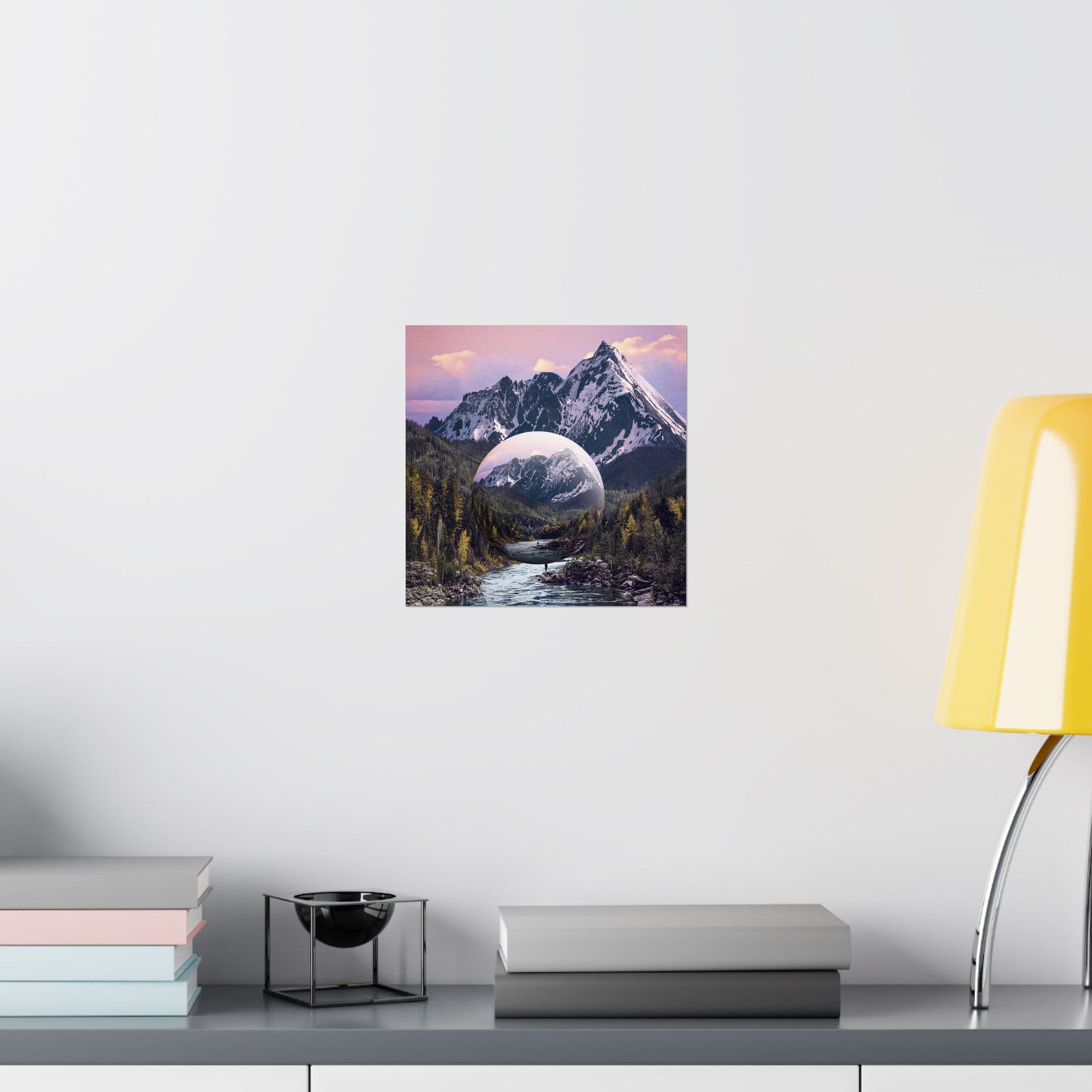 Framed artwork of a mountain landscape with a reflective lake on a white wall above a desk.
