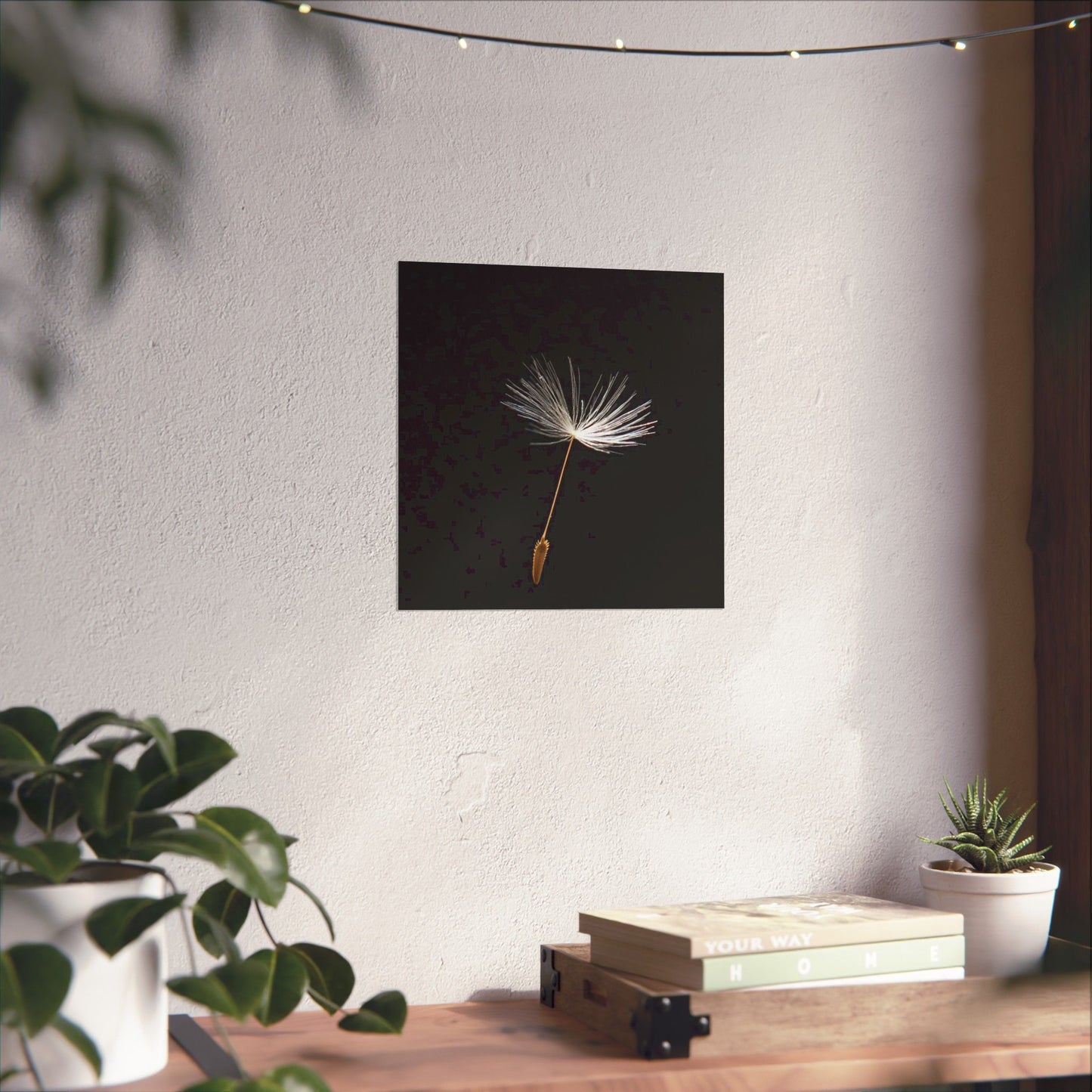 Wall art of a dandelion seed head on a white wall with plants and books below.