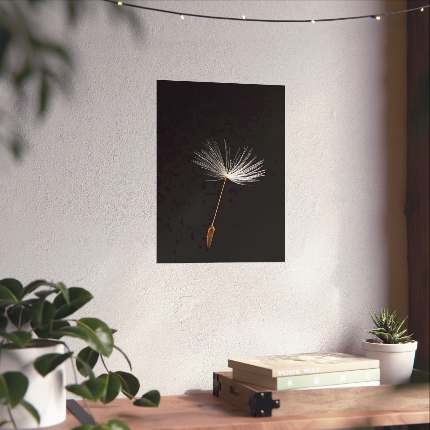 Framed artwork of a dandelion seed on a wall above a wooden table with plants.