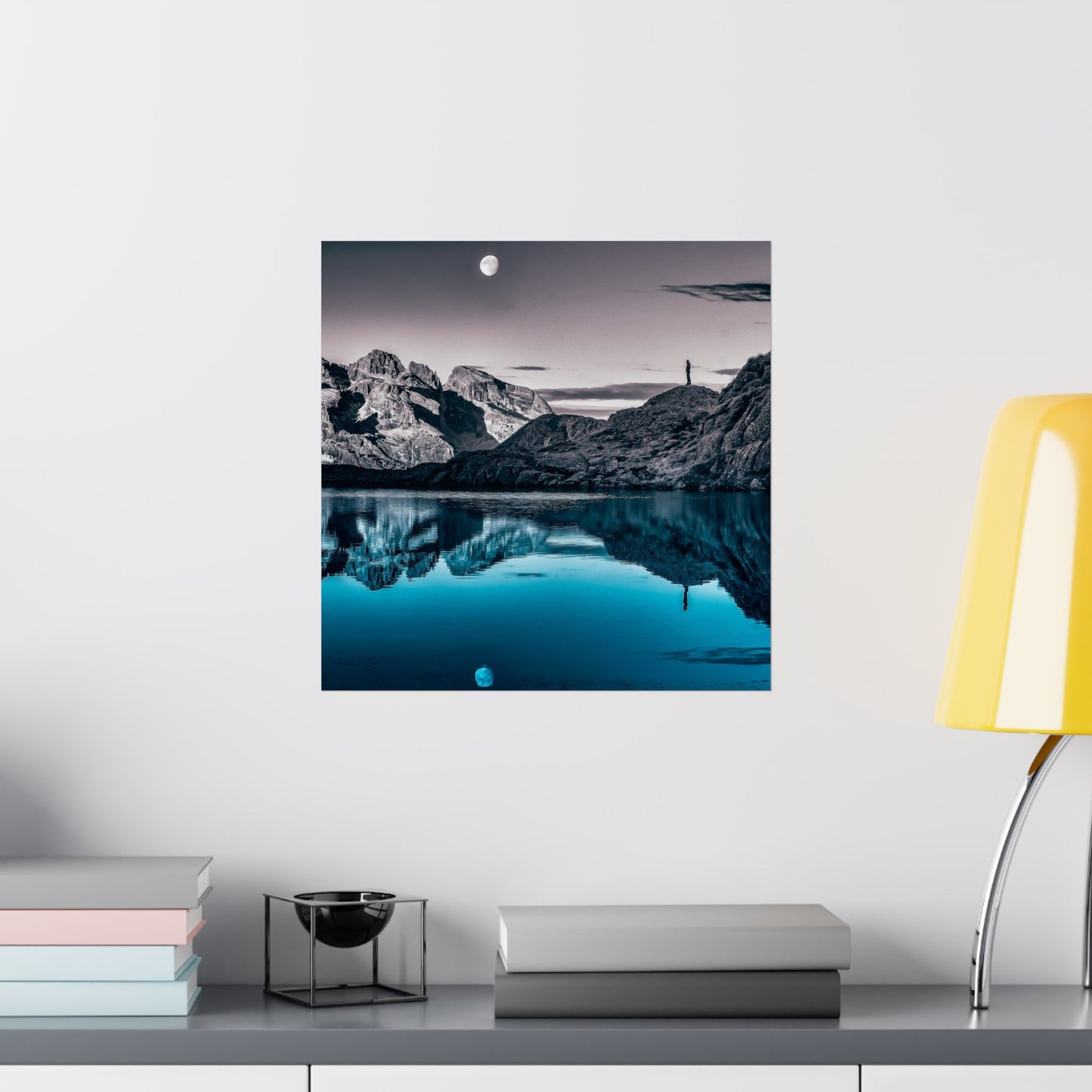 Framed mountain landscape print on a wall above a shelf with books and decor items.