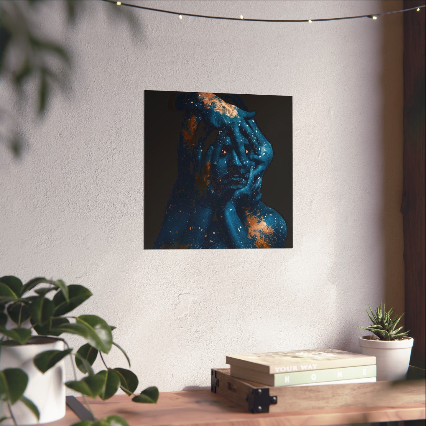 Abstract painting of a face with blue and orange hues on a white wall, with plants and books on a table below.