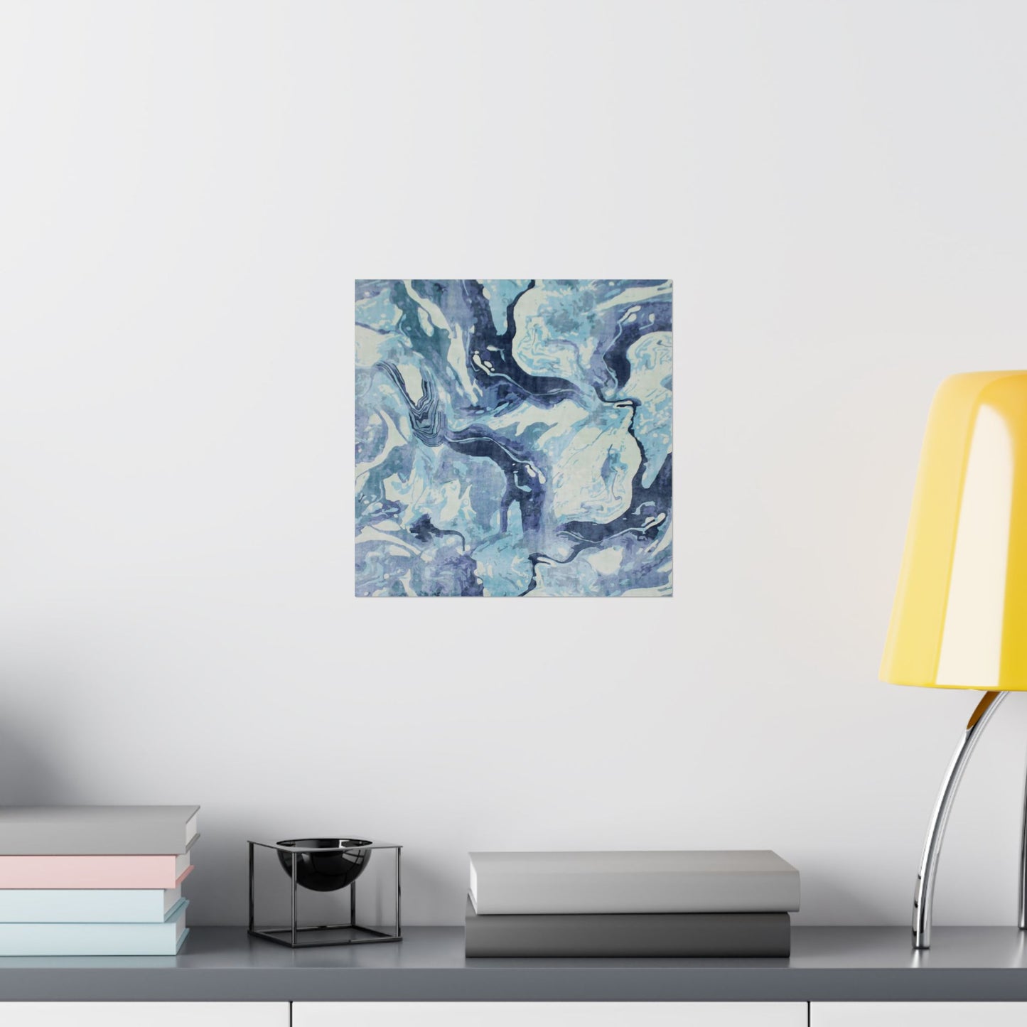 Abstract blue and white painting on a wall above a shelf with books and a lamp.