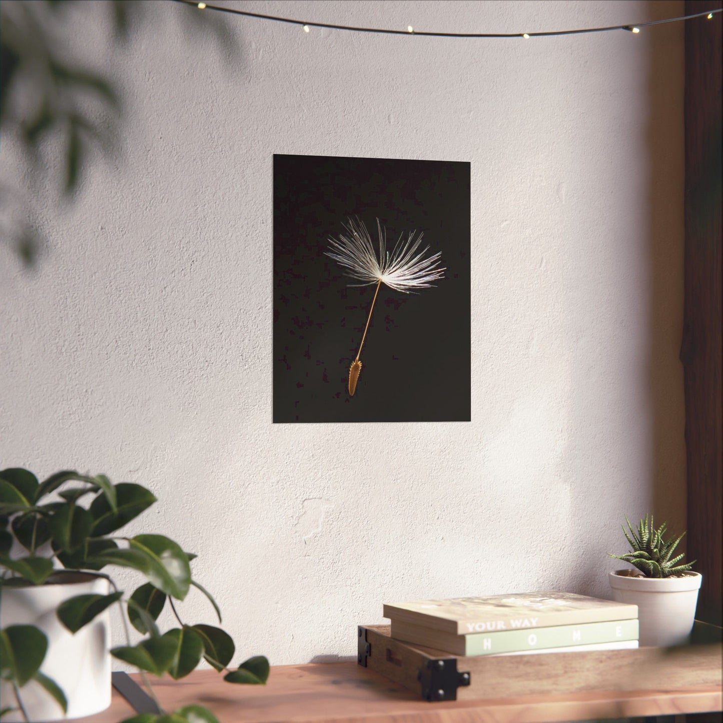 Framed artwork of a dandelion seed on a wall above a wooden table with plants.