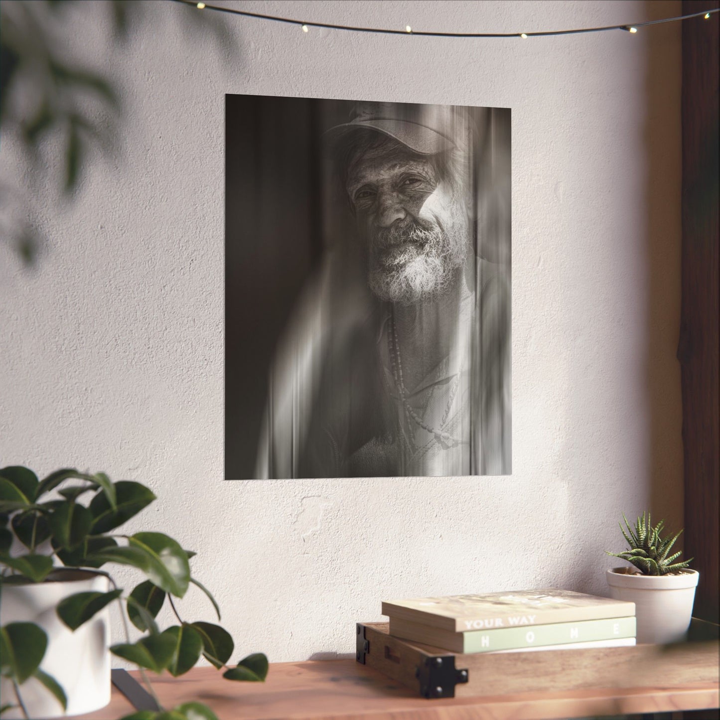 Black and white portrait of a man with a beard on a wall above a wooden desk with plants and books.