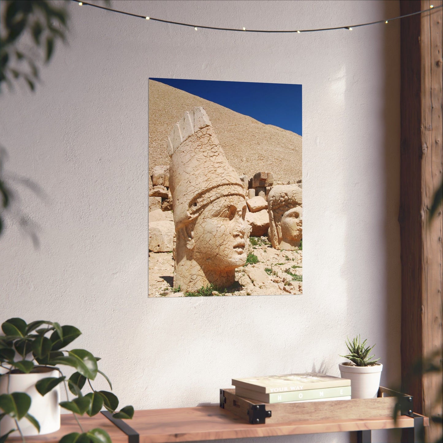 Decorative wall art of ancient stone heads on a white wall with plants and books below.