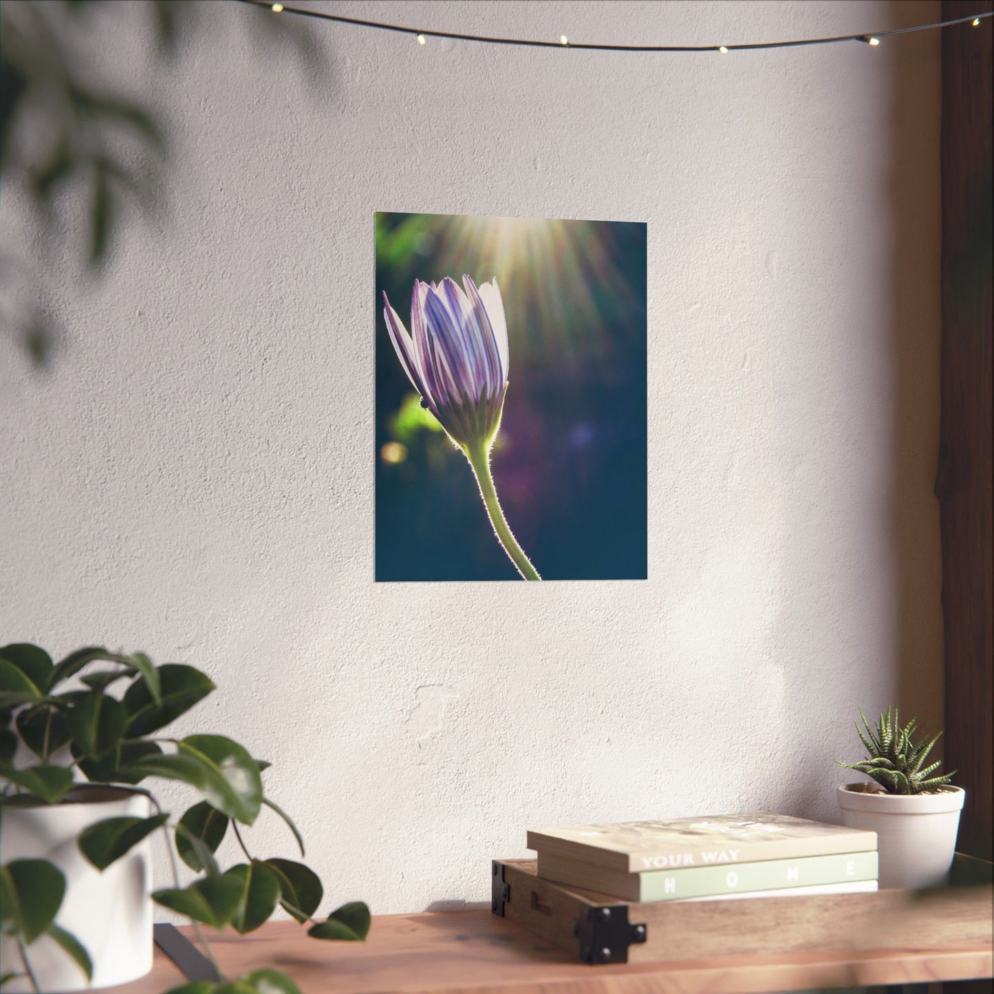 Flower poster on a wall with plants and books on a table below.
