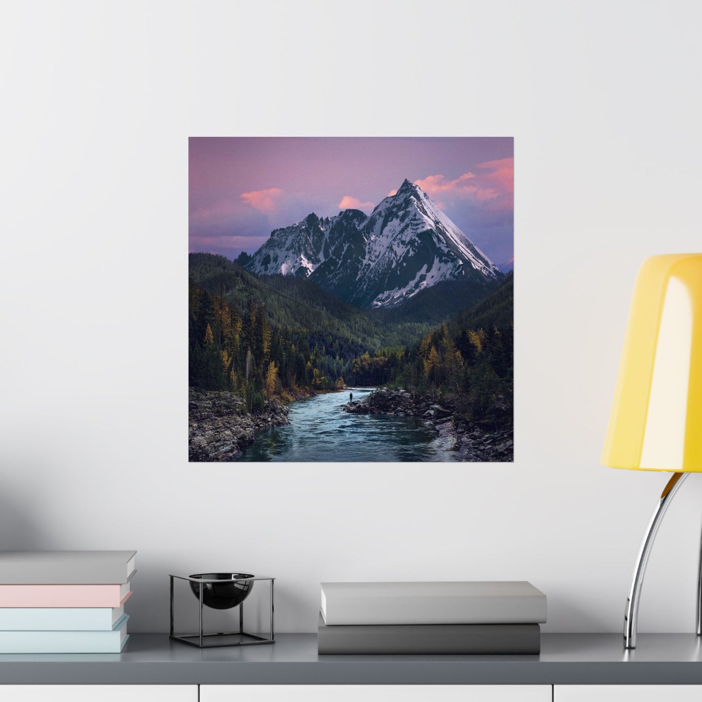 Framed mountain landscape print on a wall above a shelf with books and decor items.
