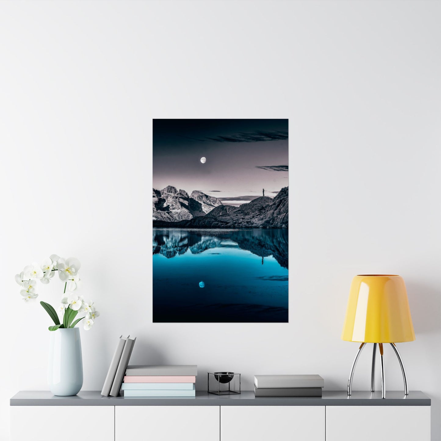 Framed mountain landscape print on a wall above a shelf with decor items.