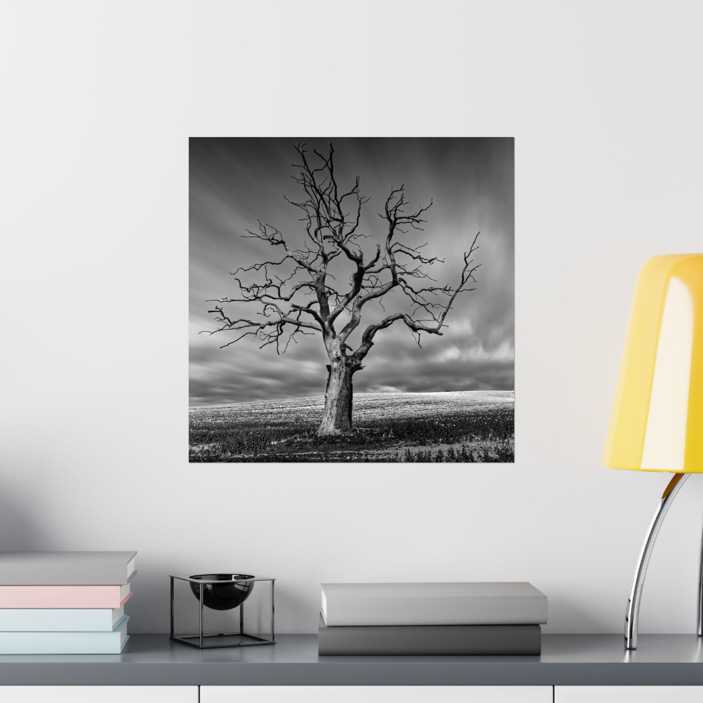 Framed black and white tree print on a wall above a shelf with books and decor items.