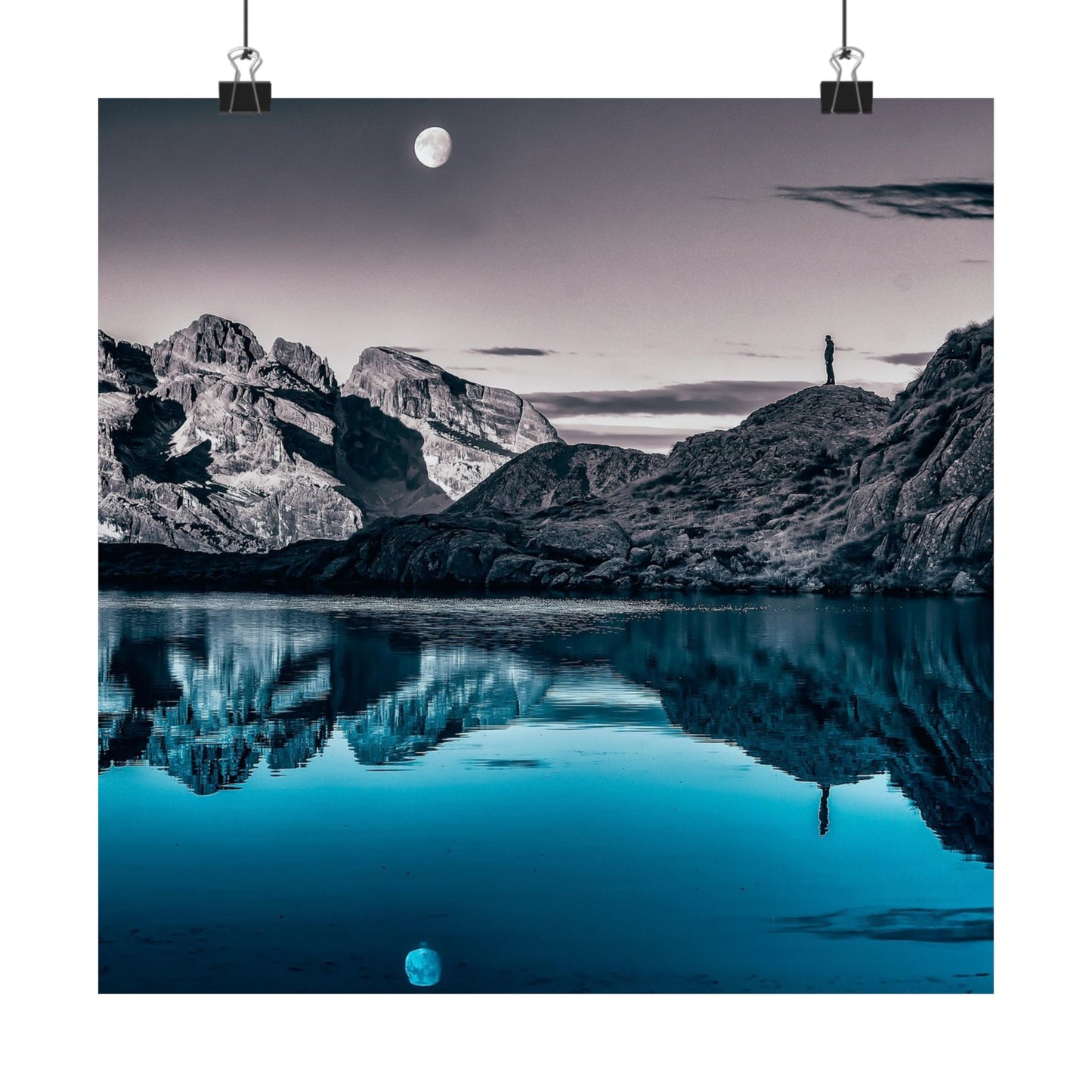 Mountain landscape with a person standing on a rock, reflecting in a calm lake under a moonlit sky.