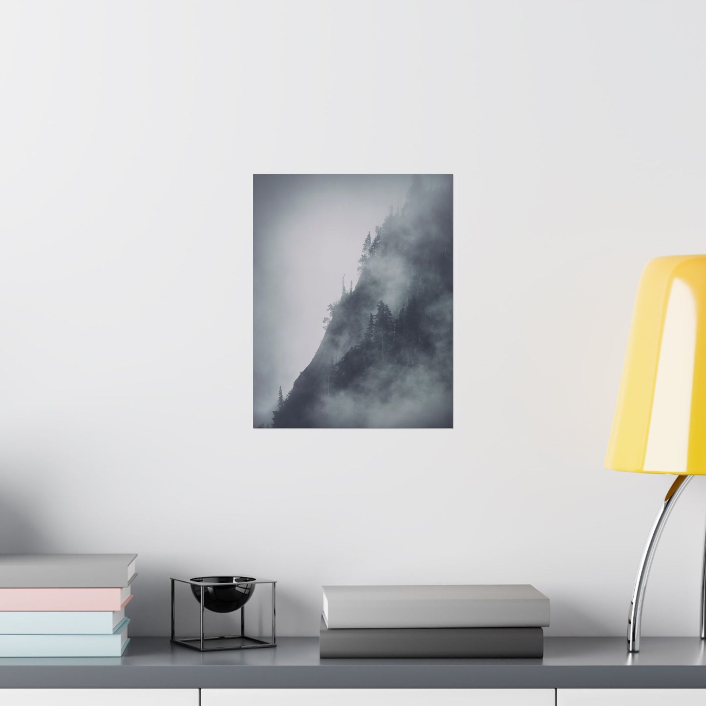 Framed artwork of a mountain landscape on a wall above a desk with books and a lamp.