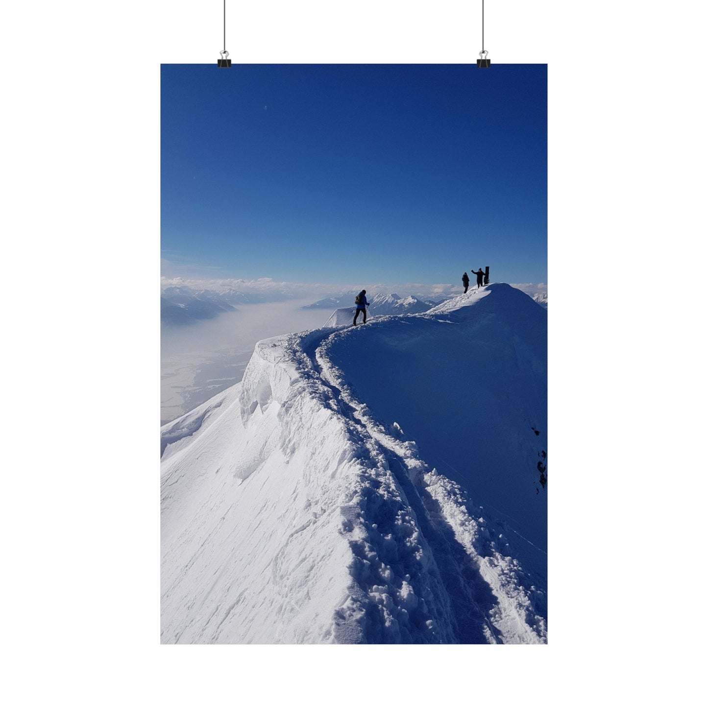 People standing on a snow-covered mountain ridge with a clear blue sky