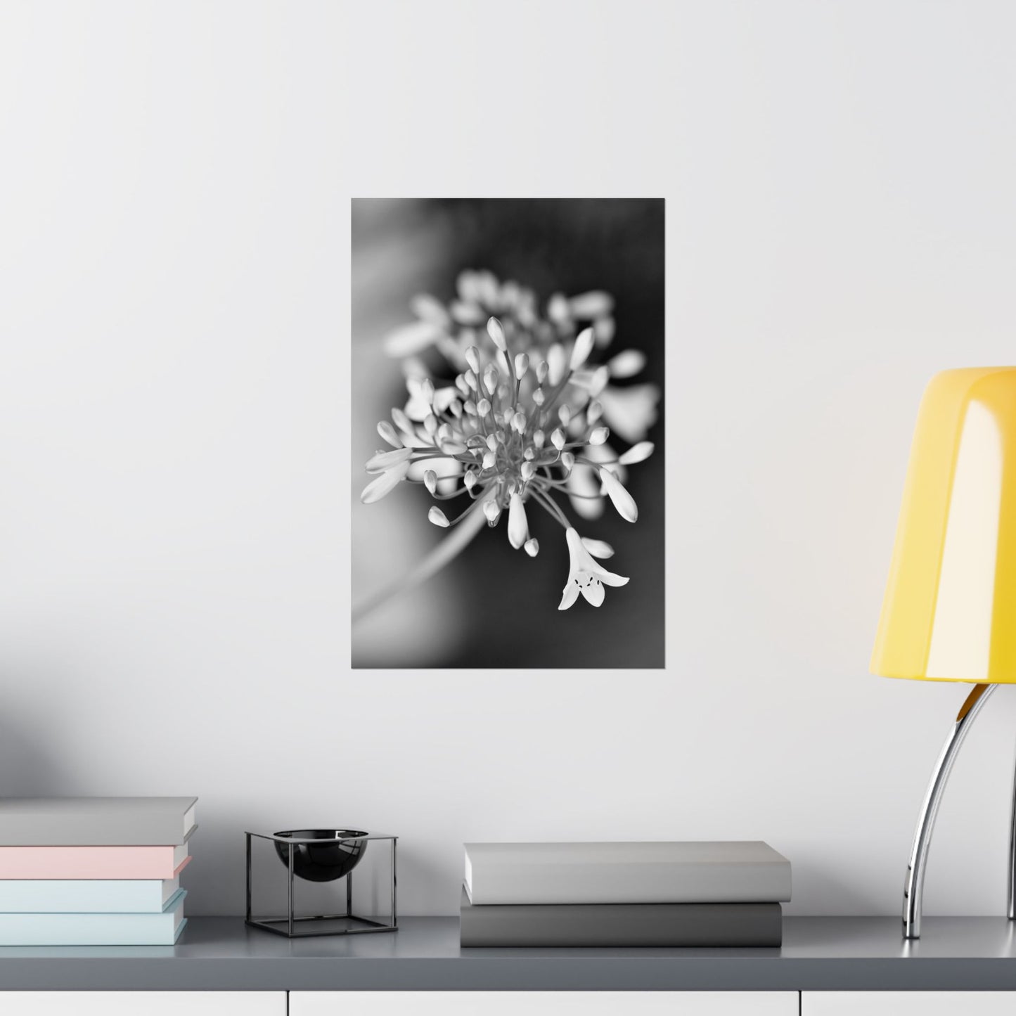 Black and white floral artwork on a wall above a shelf with books and a lamp.