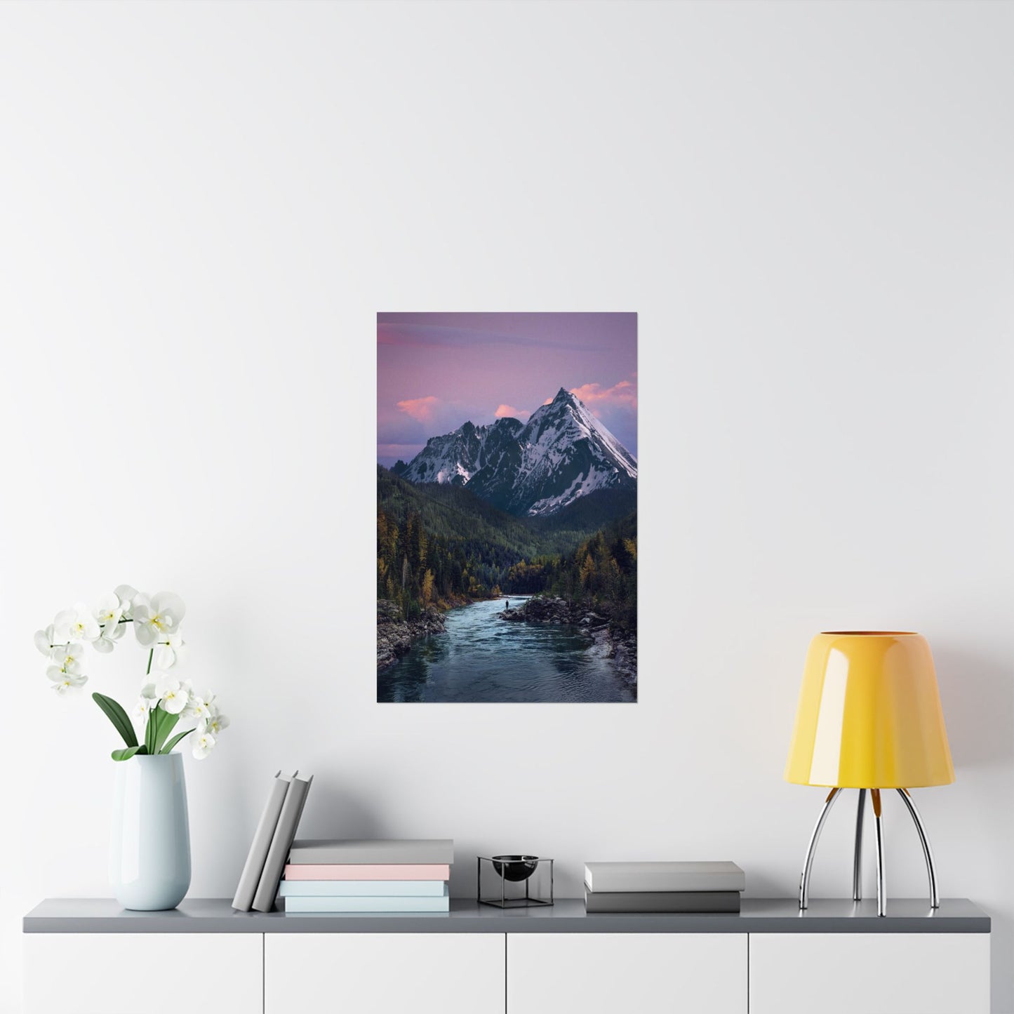 Framed mountain landscape print on a wall above a shelf with decor items.