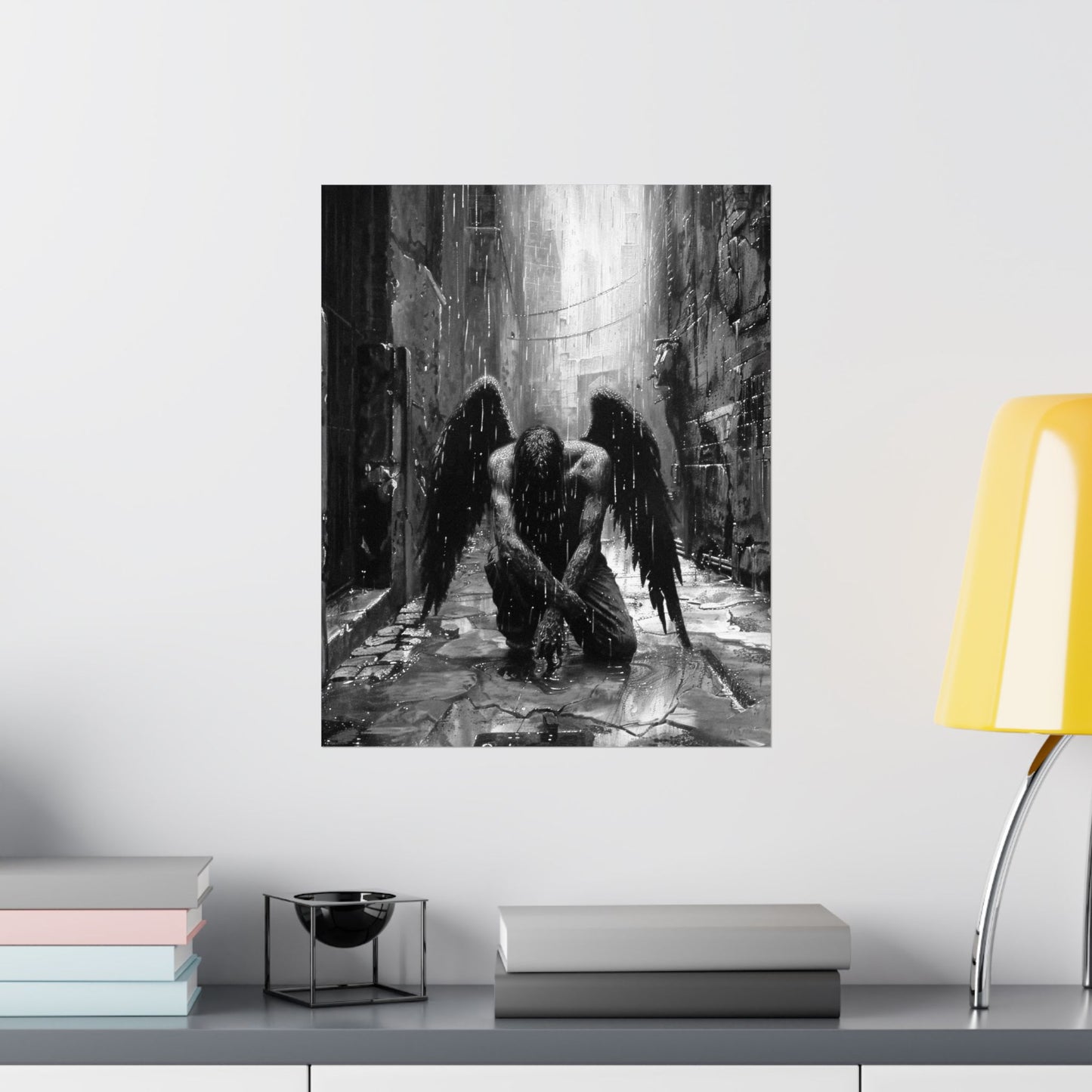 Art print of a dark angel in a gothic setting on a wall above a shelf with books and a lamp.