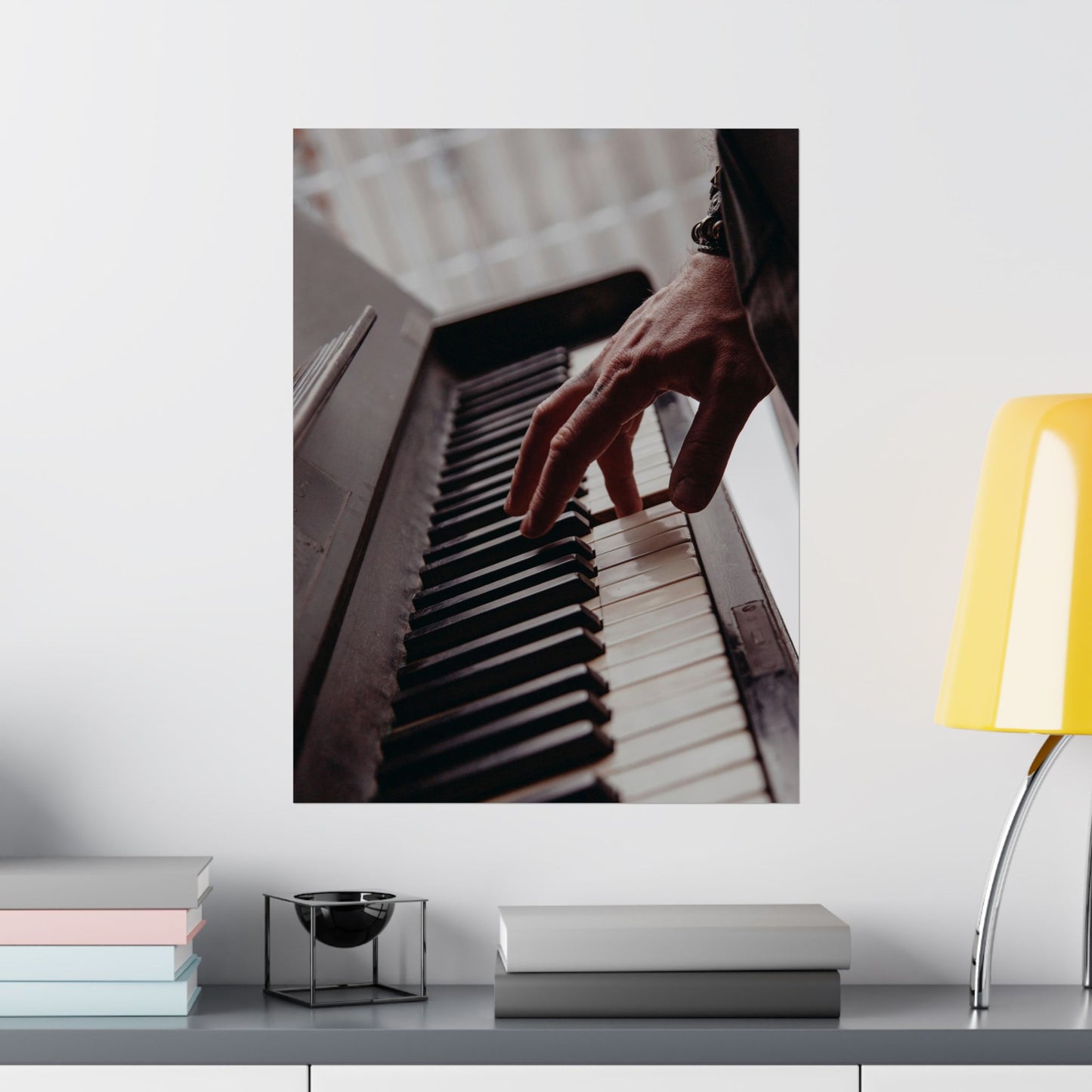 Poster of a hand playing piano on a wall above a shelf with books and decor.
