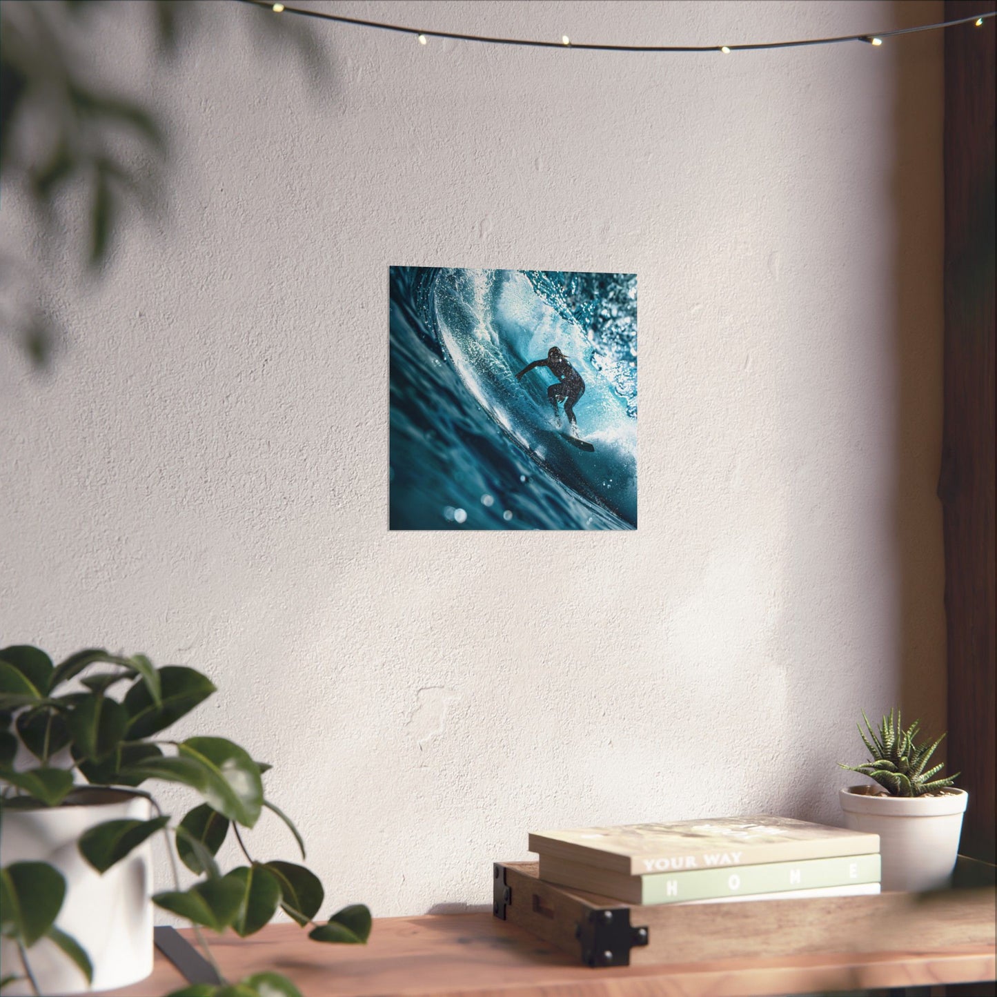 Poster of a surfer on a wave hanging on a wall above a wooden desk with plants.