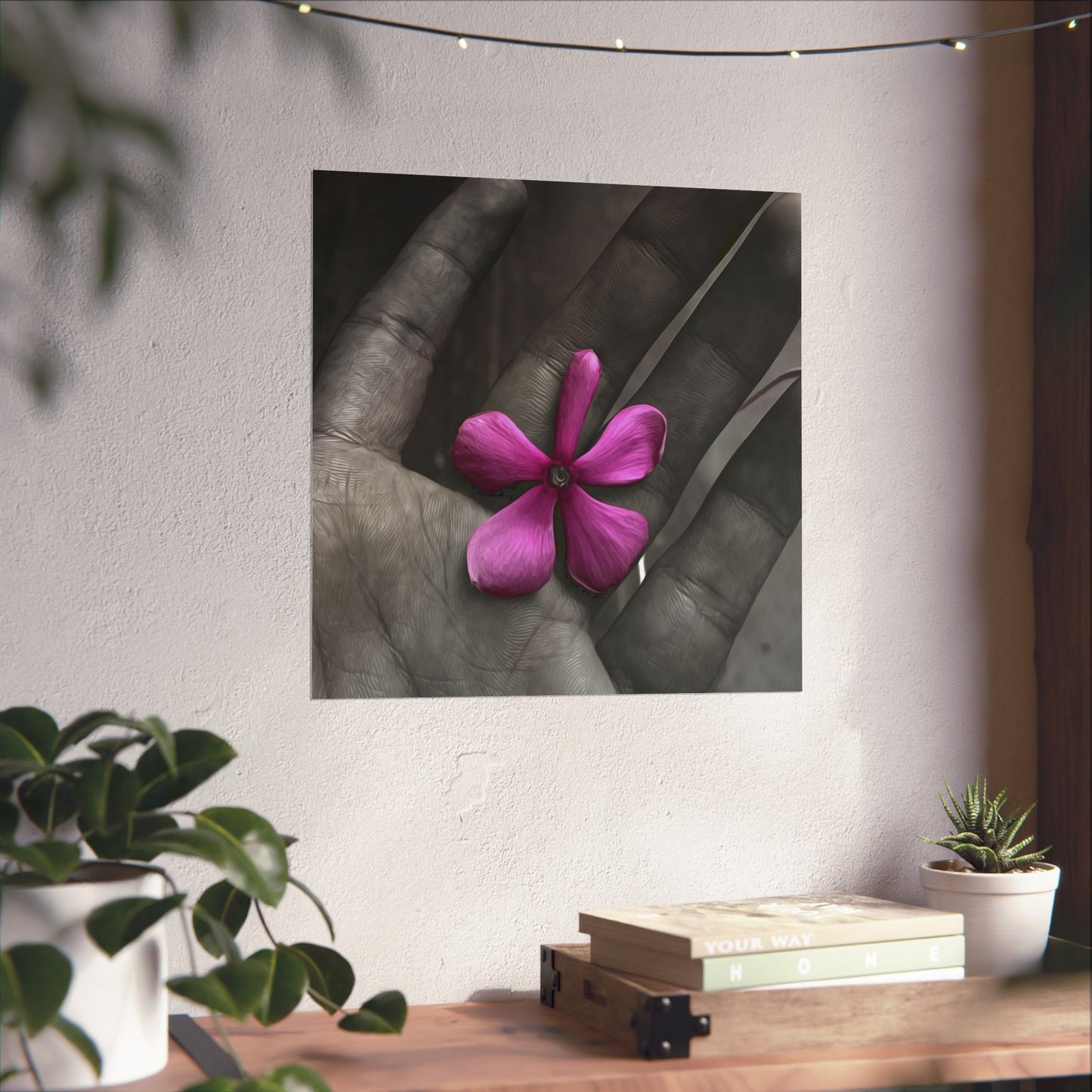 Framed artwork of a pink flower on a gray background, displayed above a desk with plants.