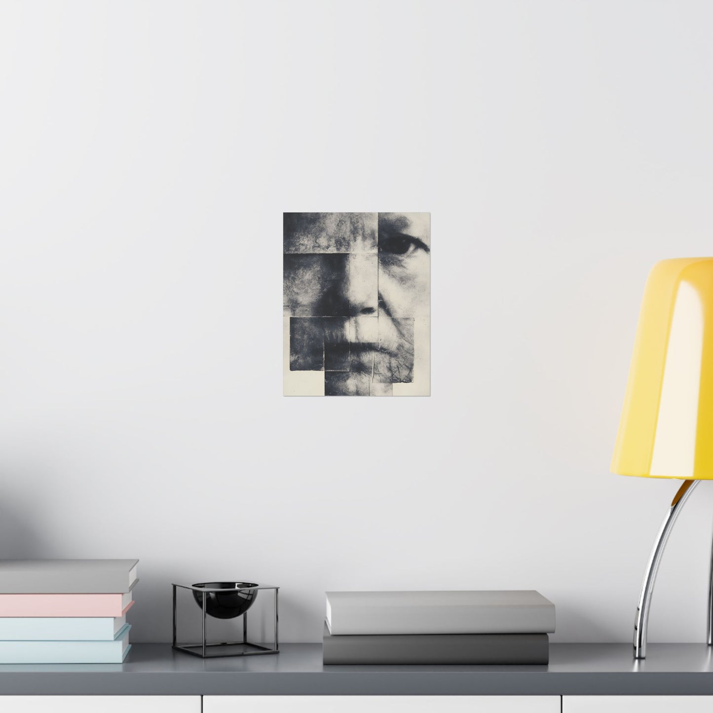 Abstract black and white portrait on a wall above a shelf with books and a lamp.