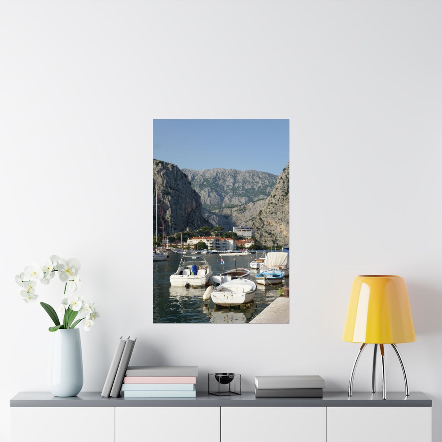 Framed photograph of a coastal scene with boats and mountains on a wall above a shelf.