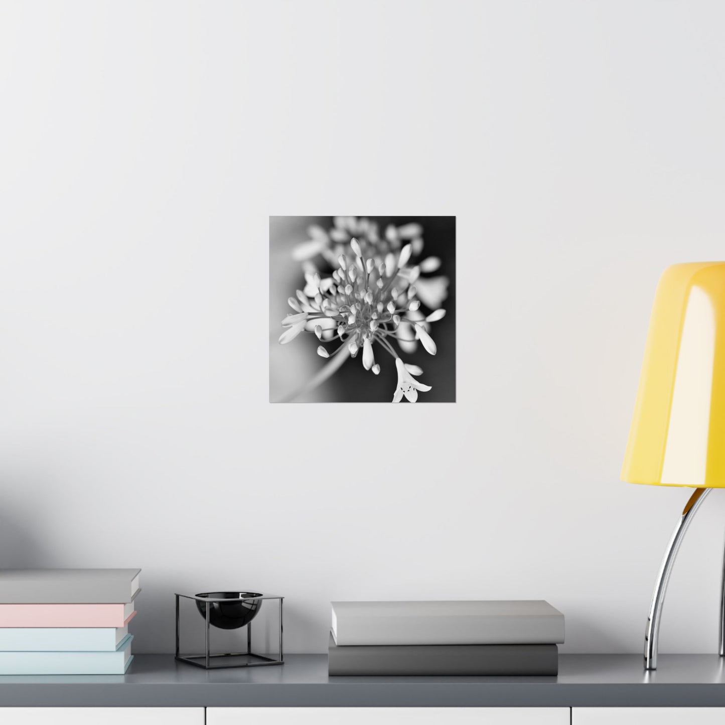 Decorative wall art of a flower on a white wall above a shelf with books and a lamp.