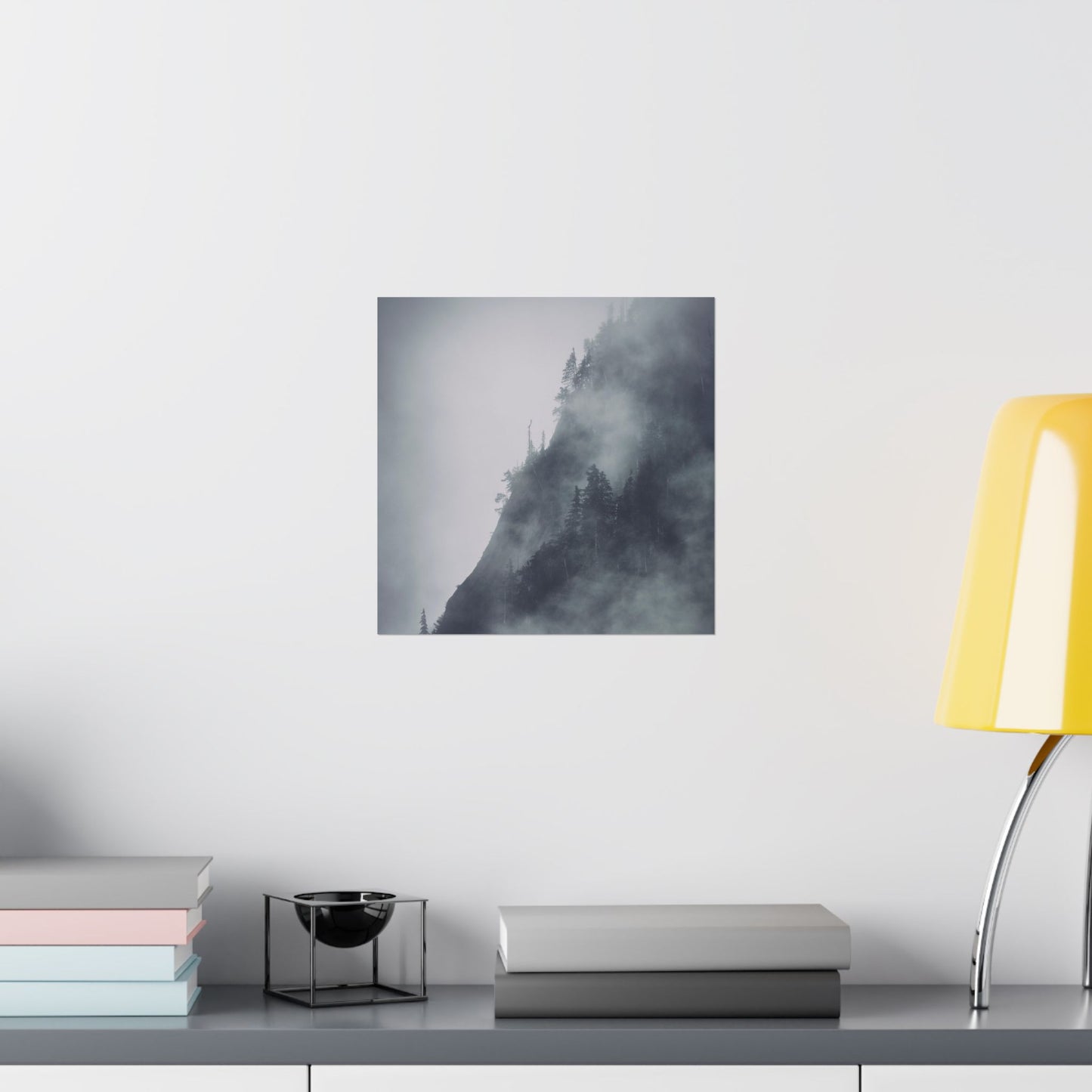 Framed abstract art piece on a wall above a desk with books and a lamp.