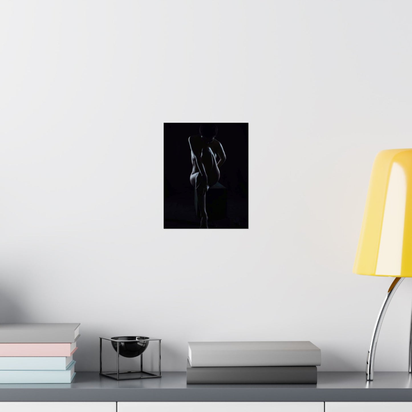 Black and white abstract art print on a white wall above a desk with books and a lamp.