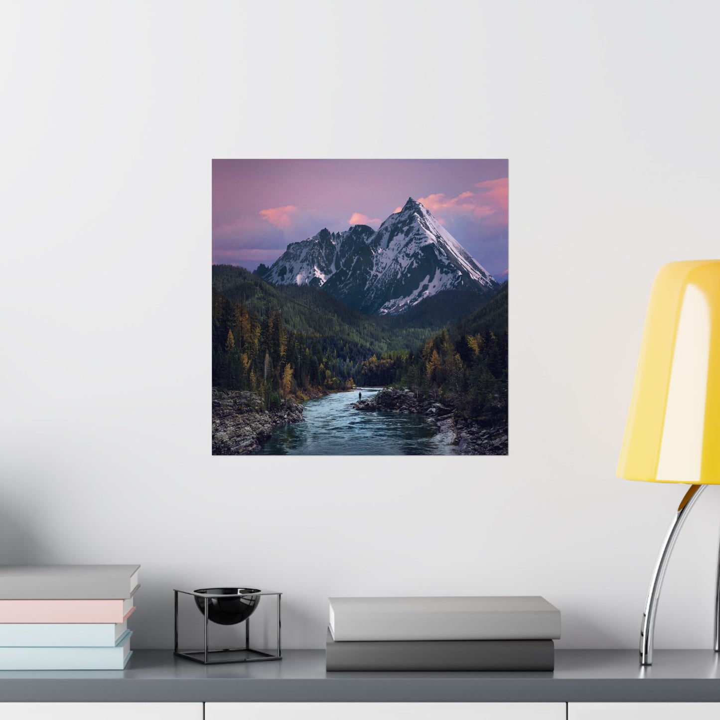Framed mountain landscape print on a wall above a shelf with books and decor.