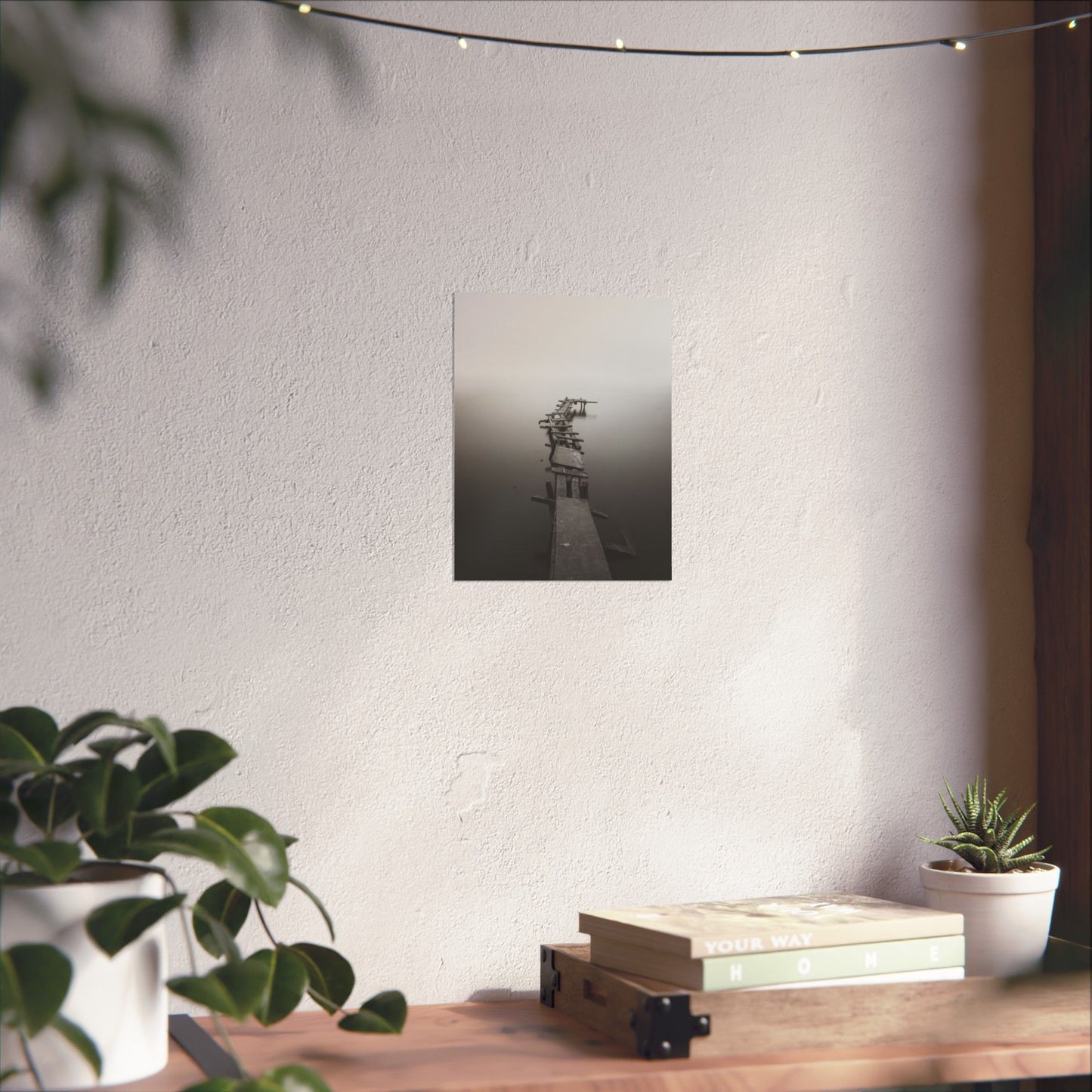 Decorative wall art on a white wall with plants and books on a wooden surface.