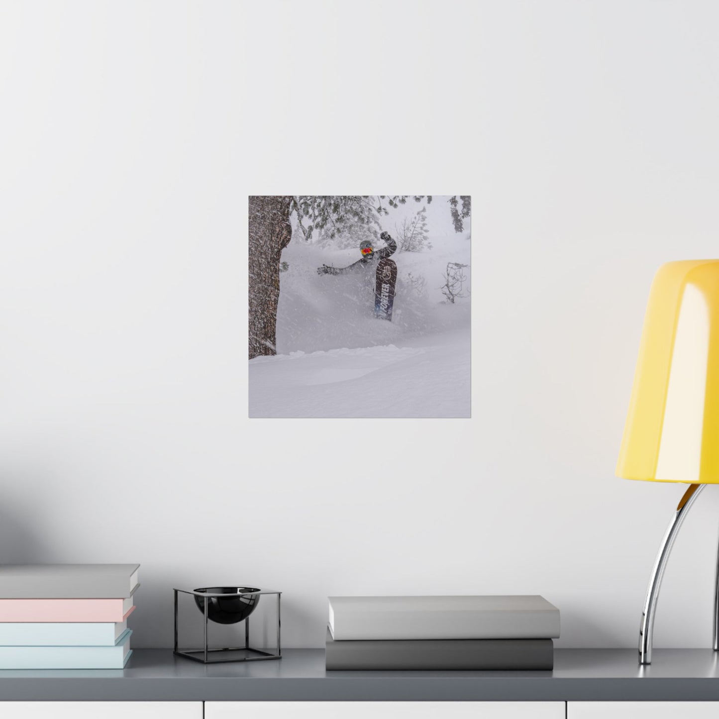 Framed photo of a person skiing on a snowy mountain wall-mounted above a desk with books and a lamp.