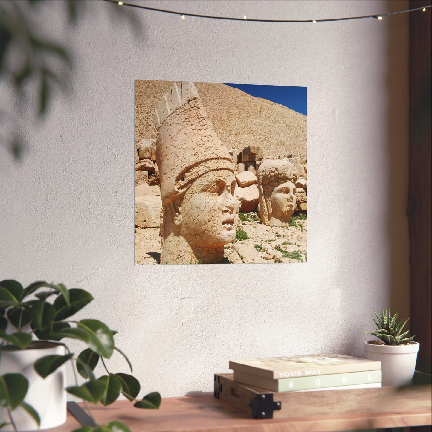 Framed artwork of stone heads on a wall above a desk with plants.