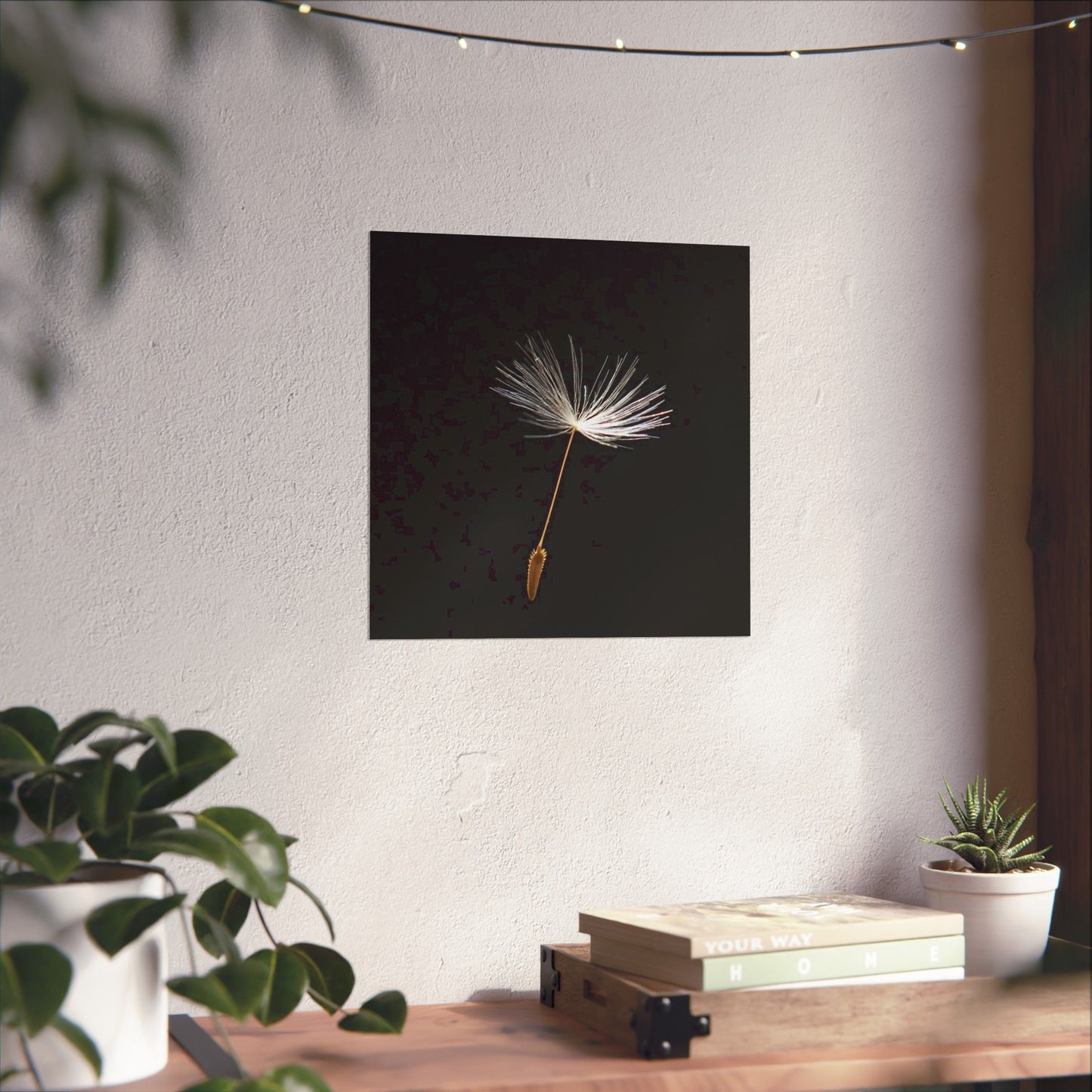 Wall art of a dandelion seed head on a black background in a room with plants and books.