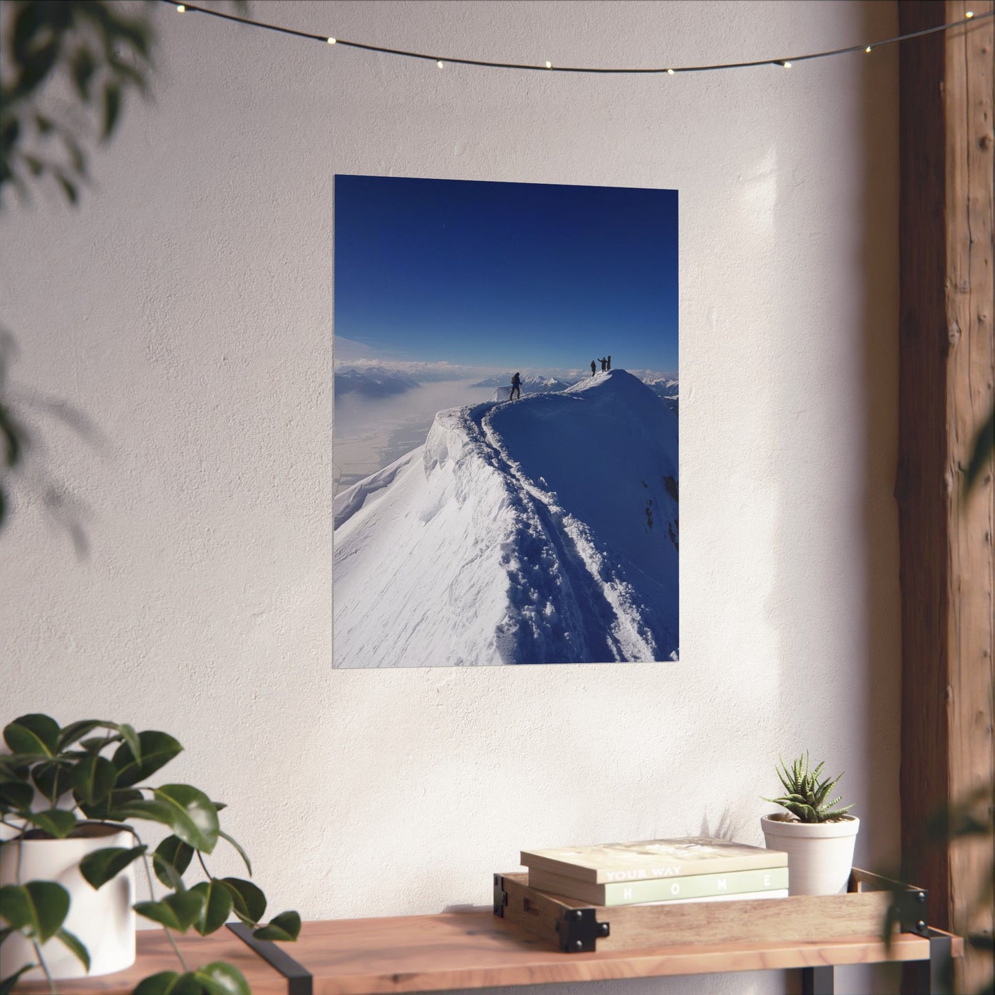 Framed photograph of a snowy mountain landscape on a wall above a wooden shelf with books and plants.
