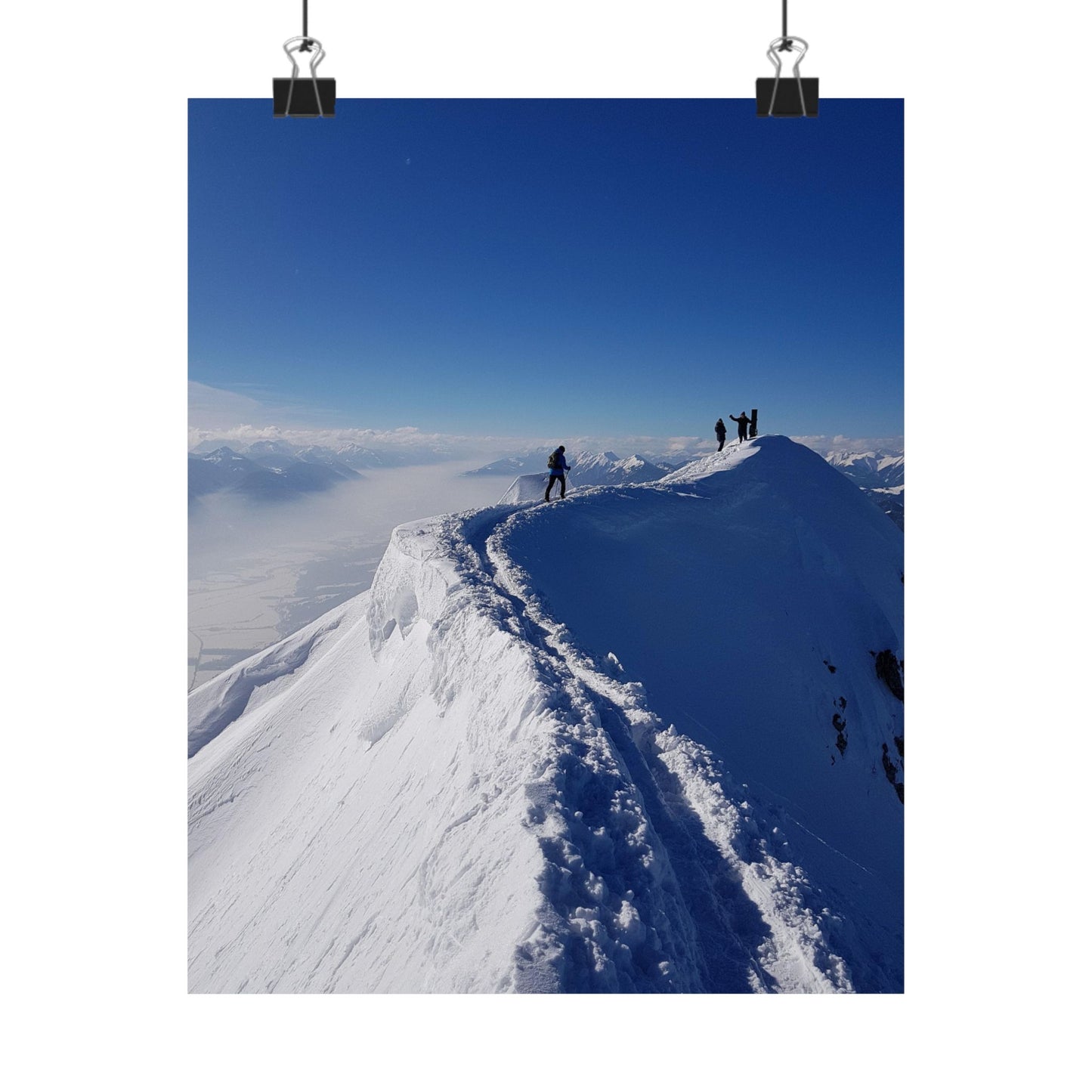 Two people standing on a snowy mountain peak with a clear blue sky.