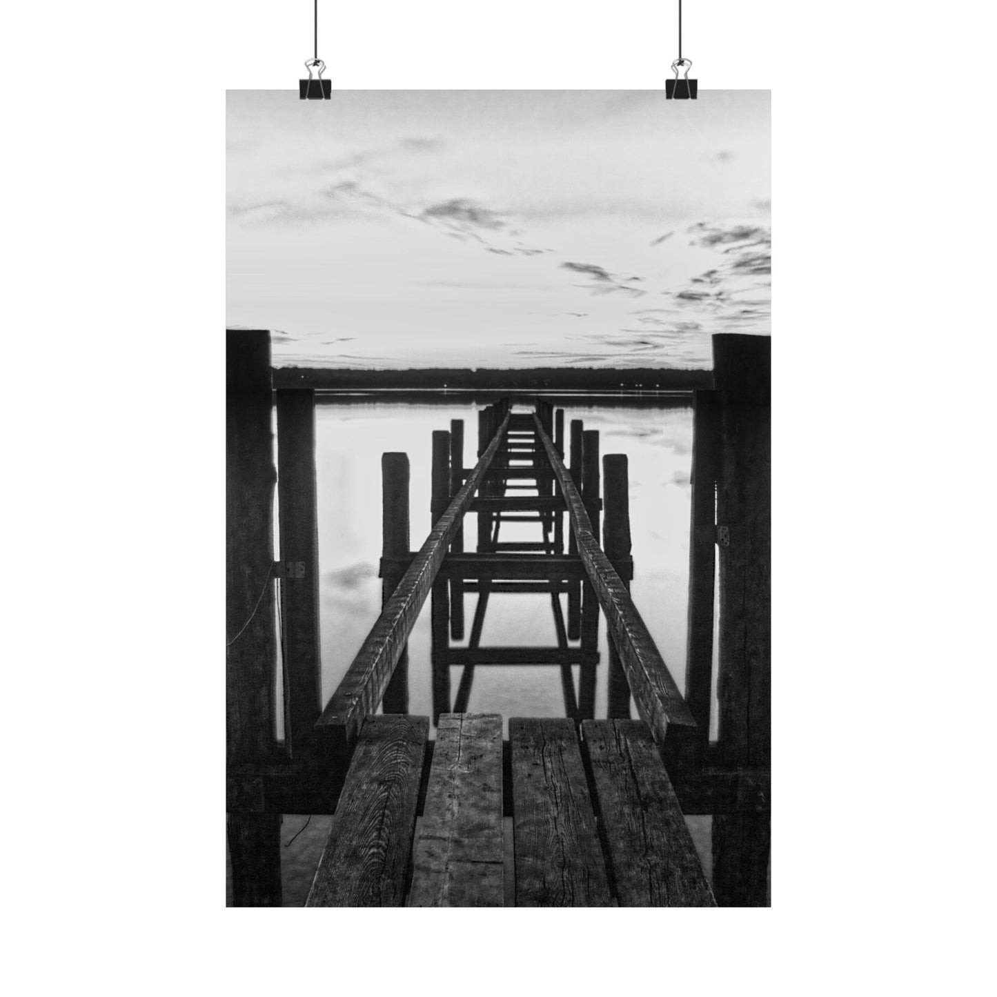 Black and white photo of a wooden pier extending into water with a cloudy sky.