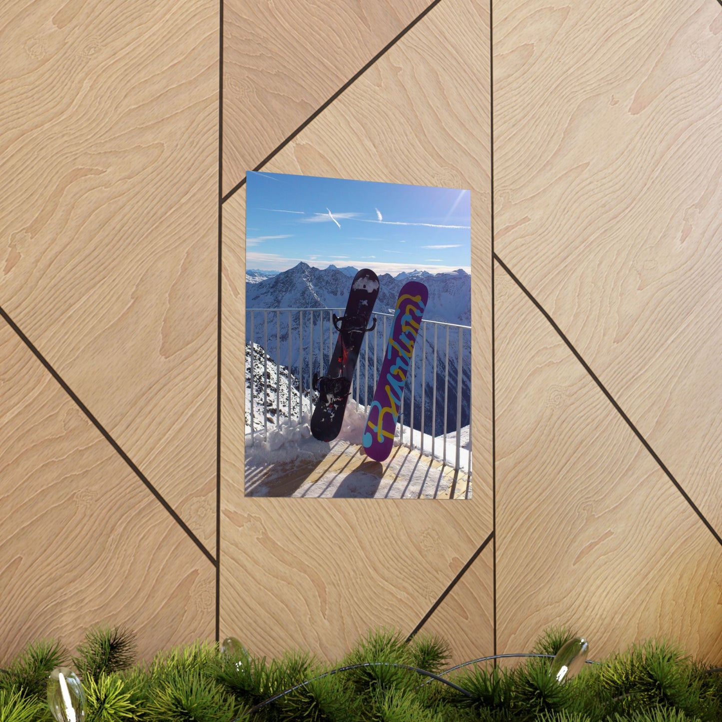 Two snowboards leaning against a railing with mountains in the background, displayed on a wooden panel.