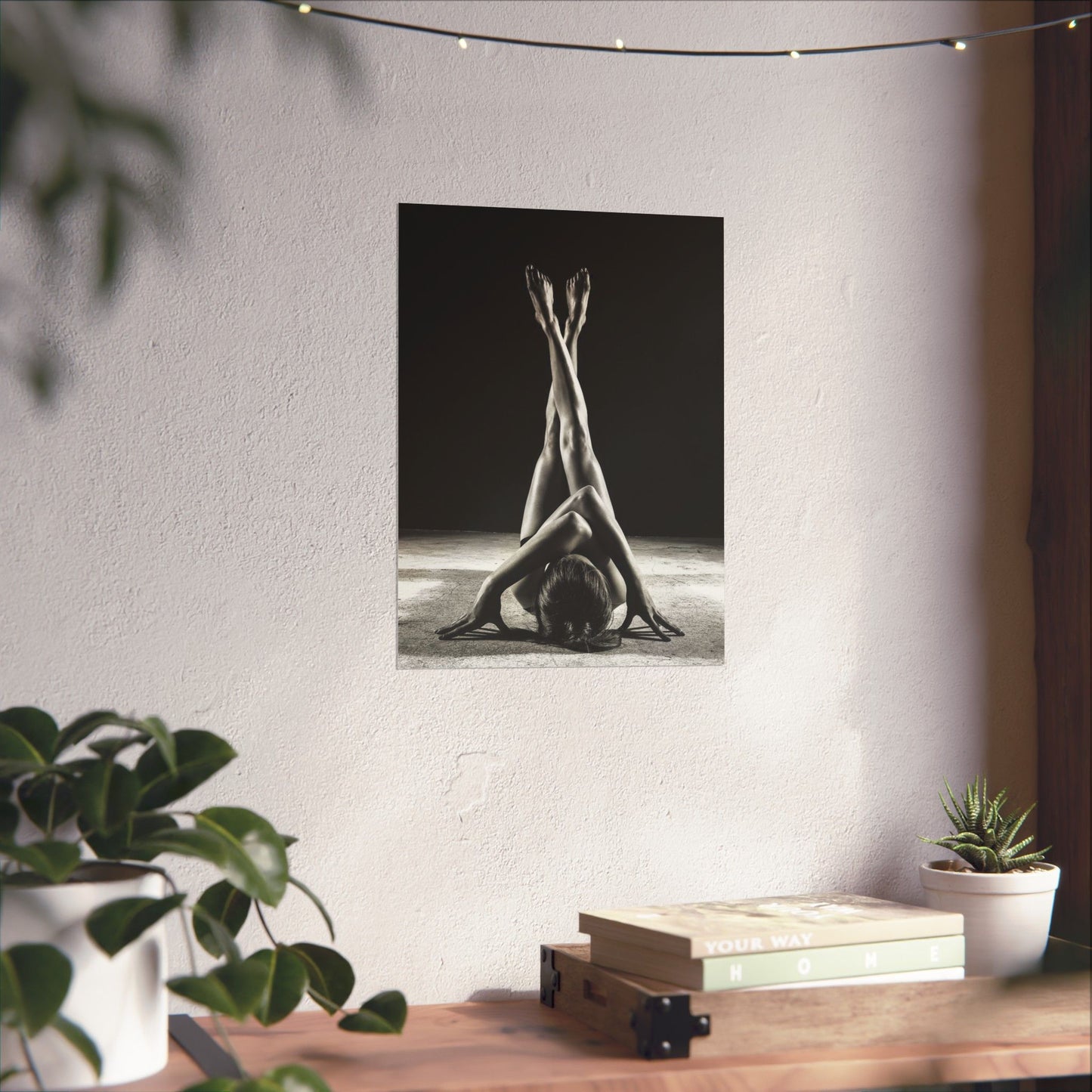 Poster of a yoga pose on a wall with plants and books on a table below.
