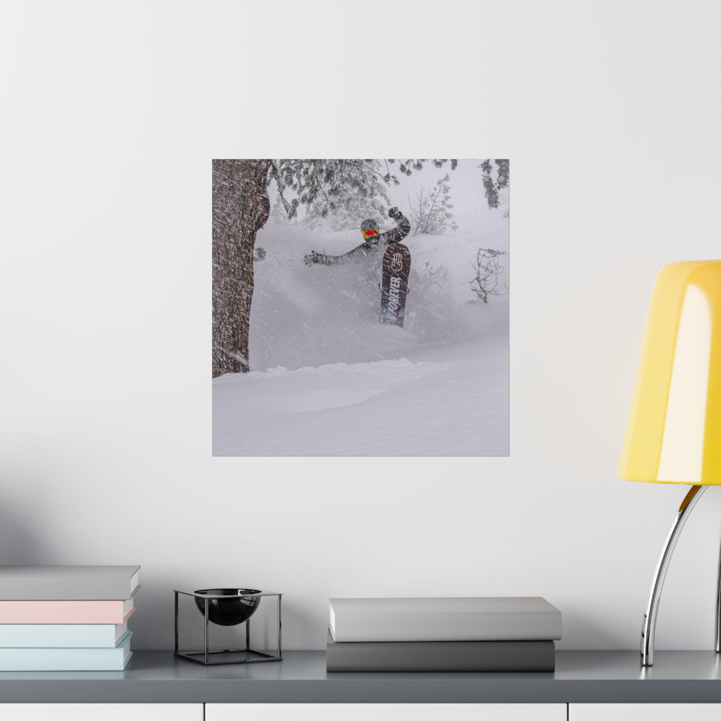 Poster of a person skiing in the snow on a wall above a desk with books and a lamp.