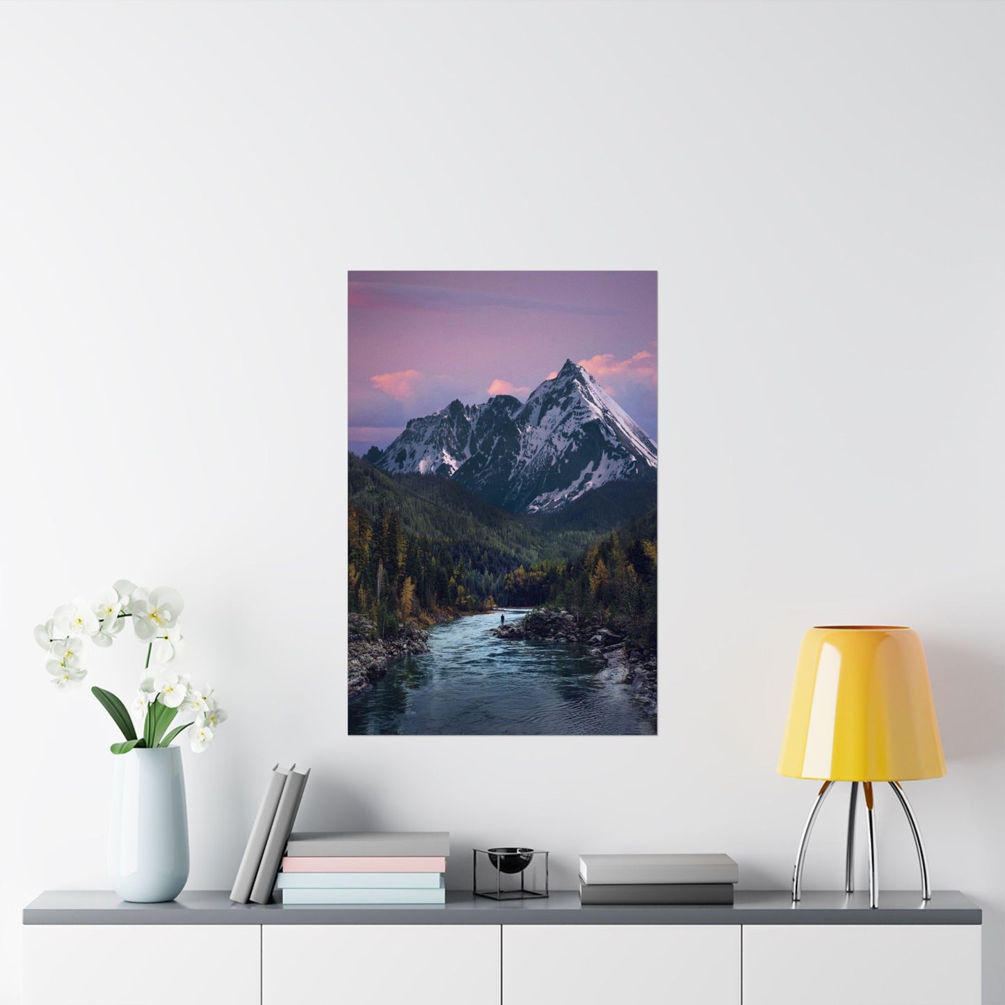 Framed mountain landscape print on a wall above a table with decor items.