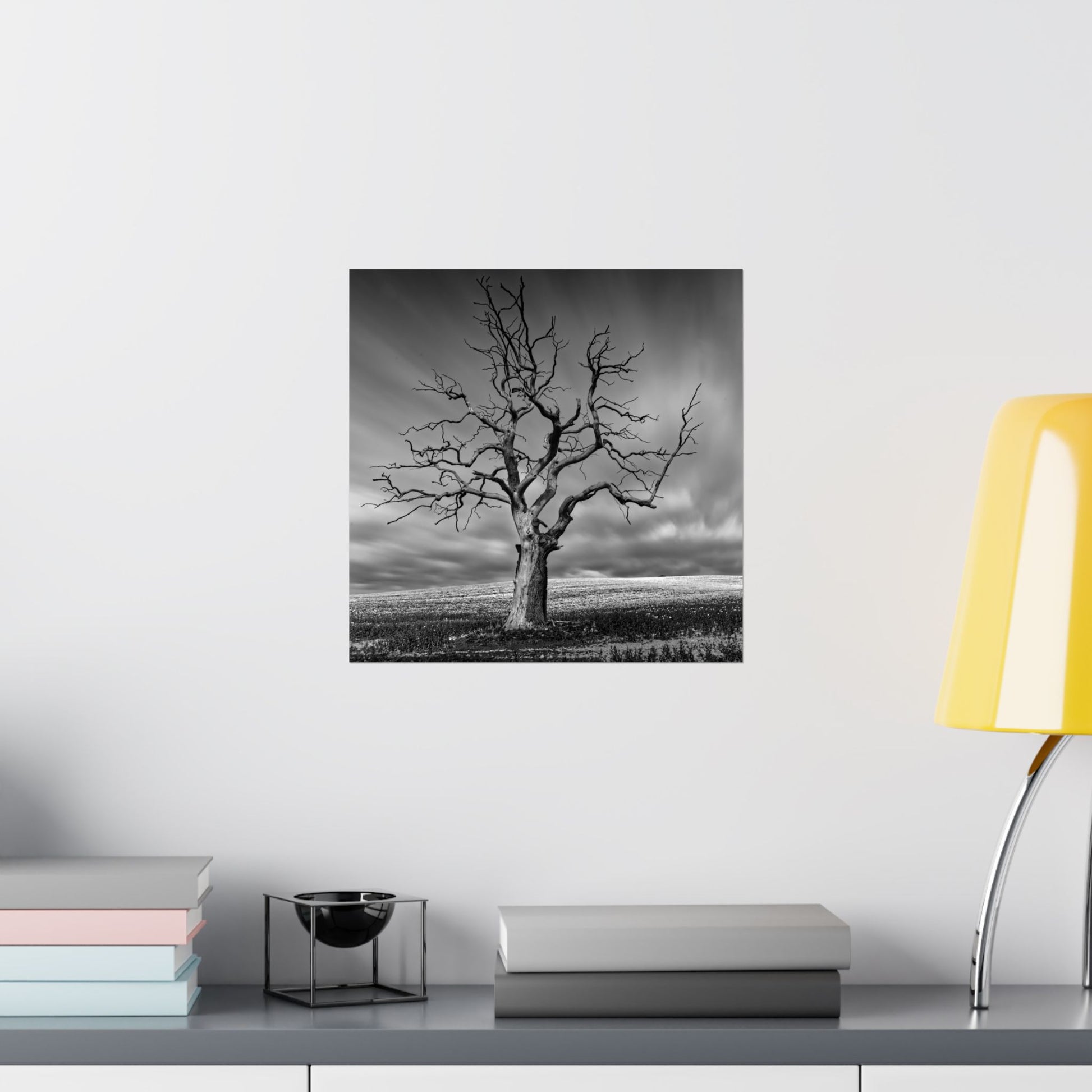 Black and white tree artwork on a wall above a shelf with books and a lamp.