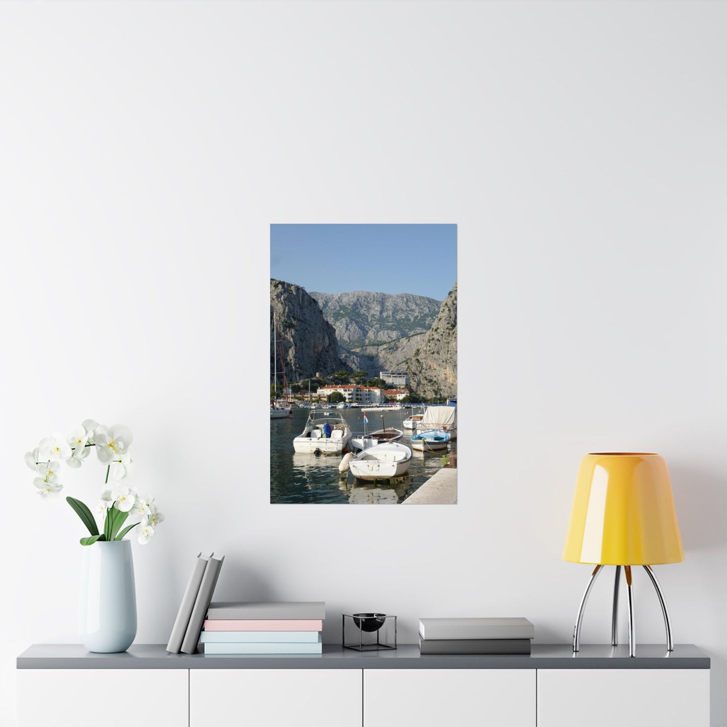 Framed photograph of a coastal scene with boats on a wall above a shelf with decor items.