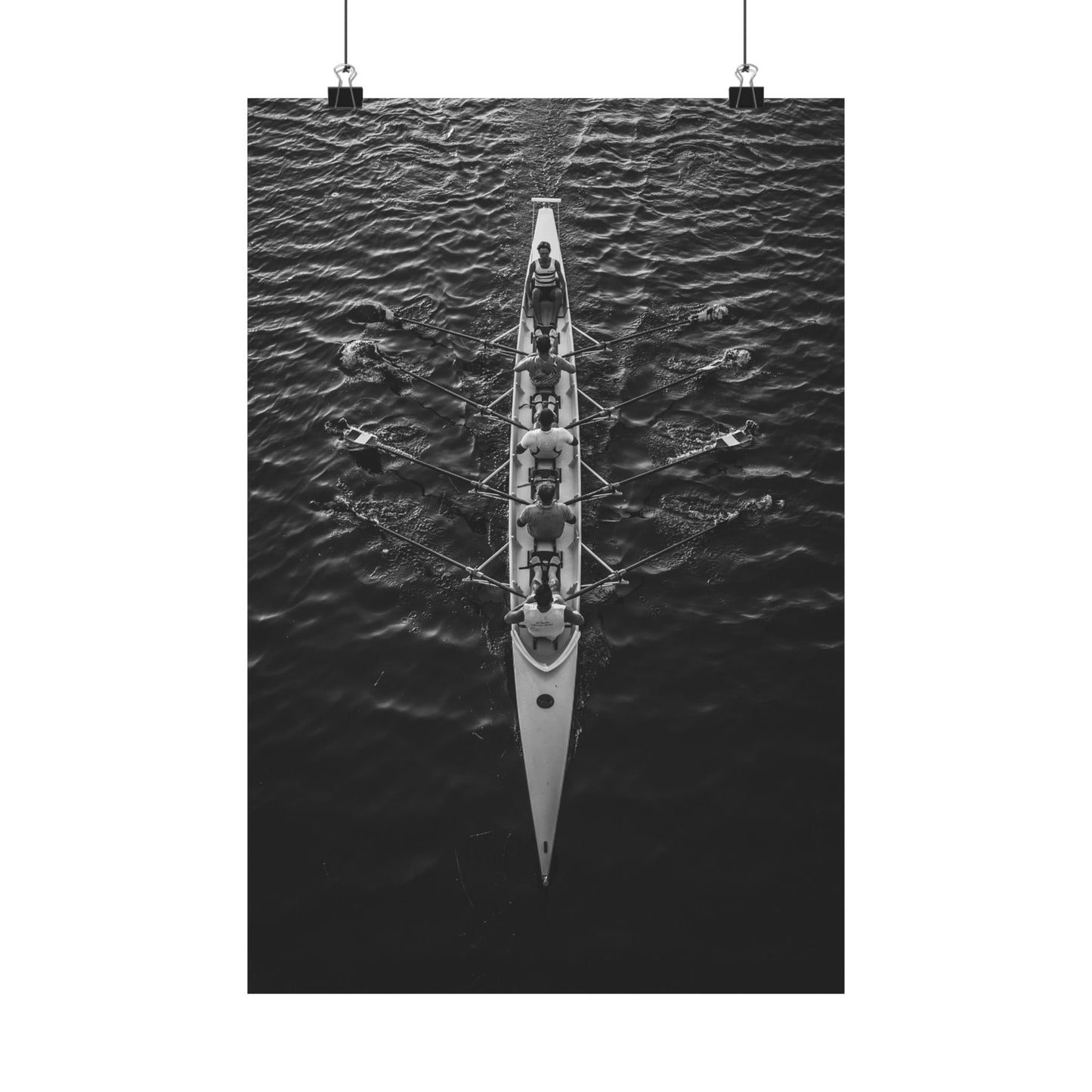 Black and white photograph of a rowing boat with multiple rowers on water.
