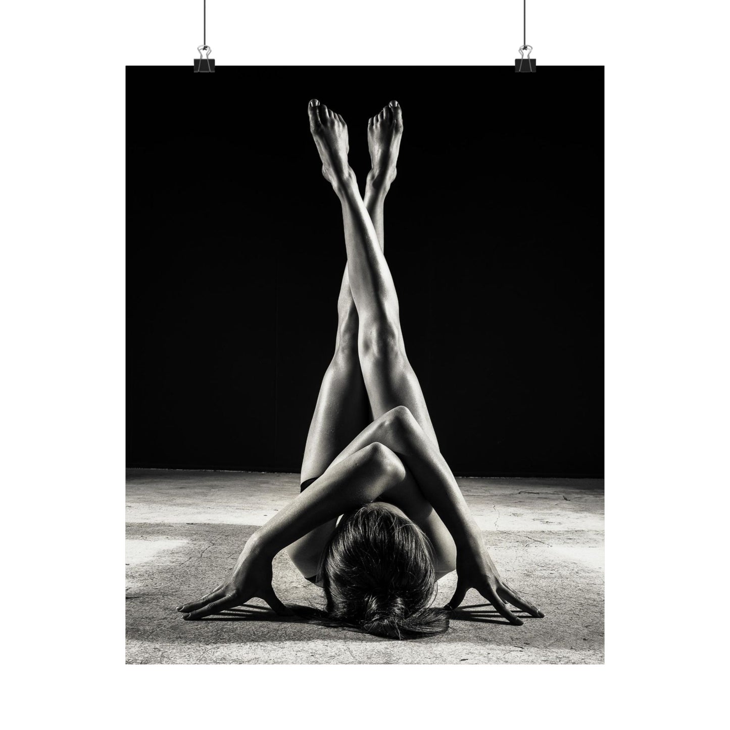 Black and white photo of a person in a yoga pose with feet in the air against a dark background.