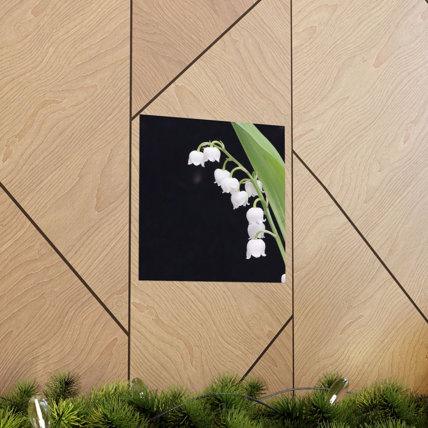 Framed artwork of white flowers on a wooden wall with greenery at the bottom.