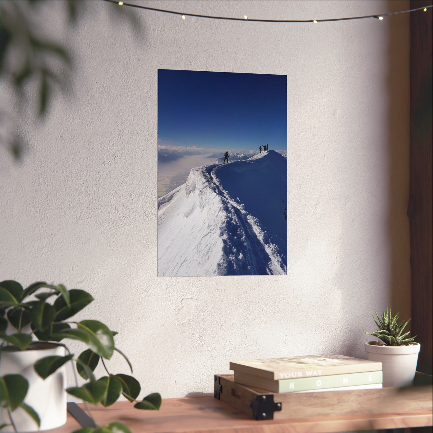 Poster of a snowy mountain landscape on a wall above a desk with plants and books.