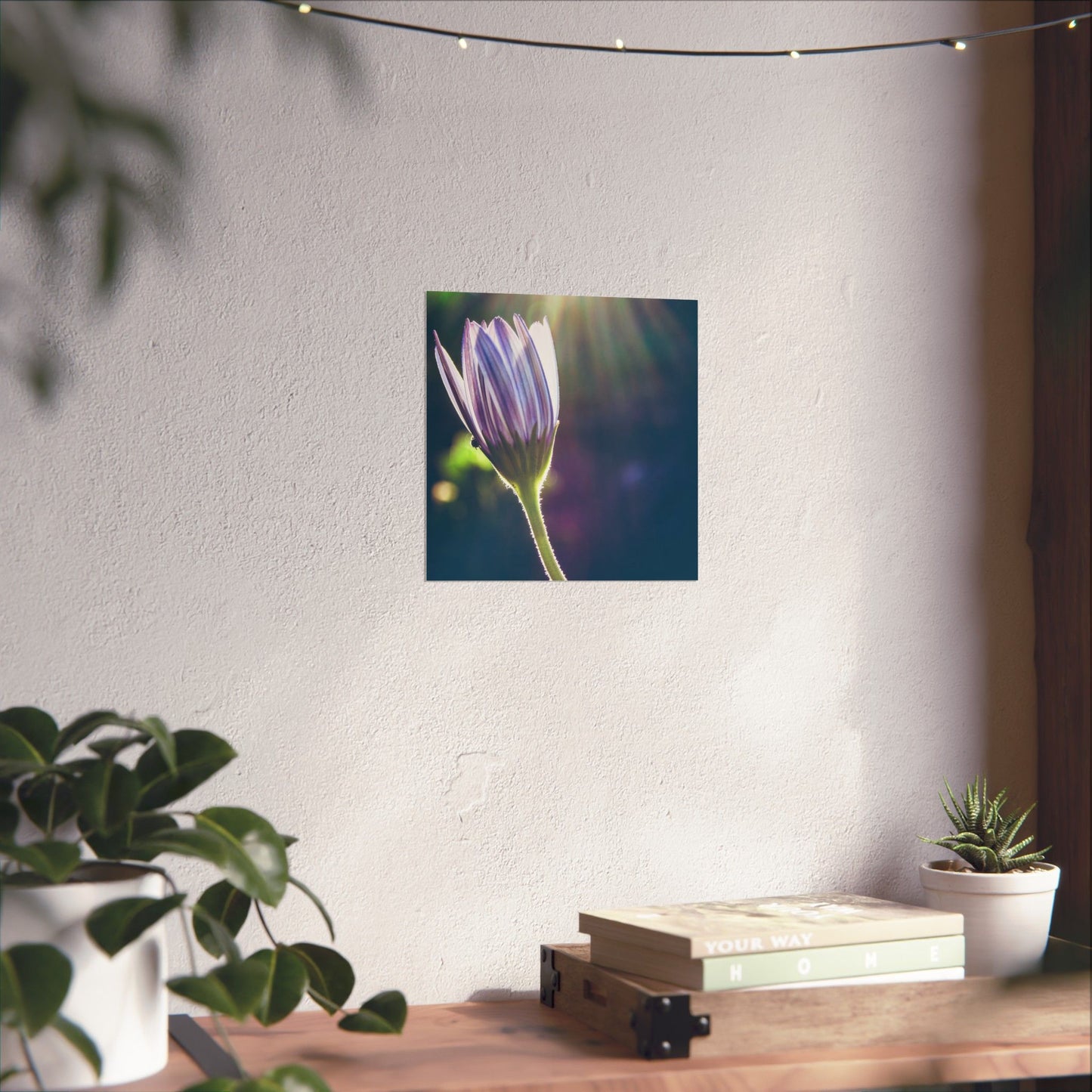 Flower poster on a wall with plants and books on a table below.