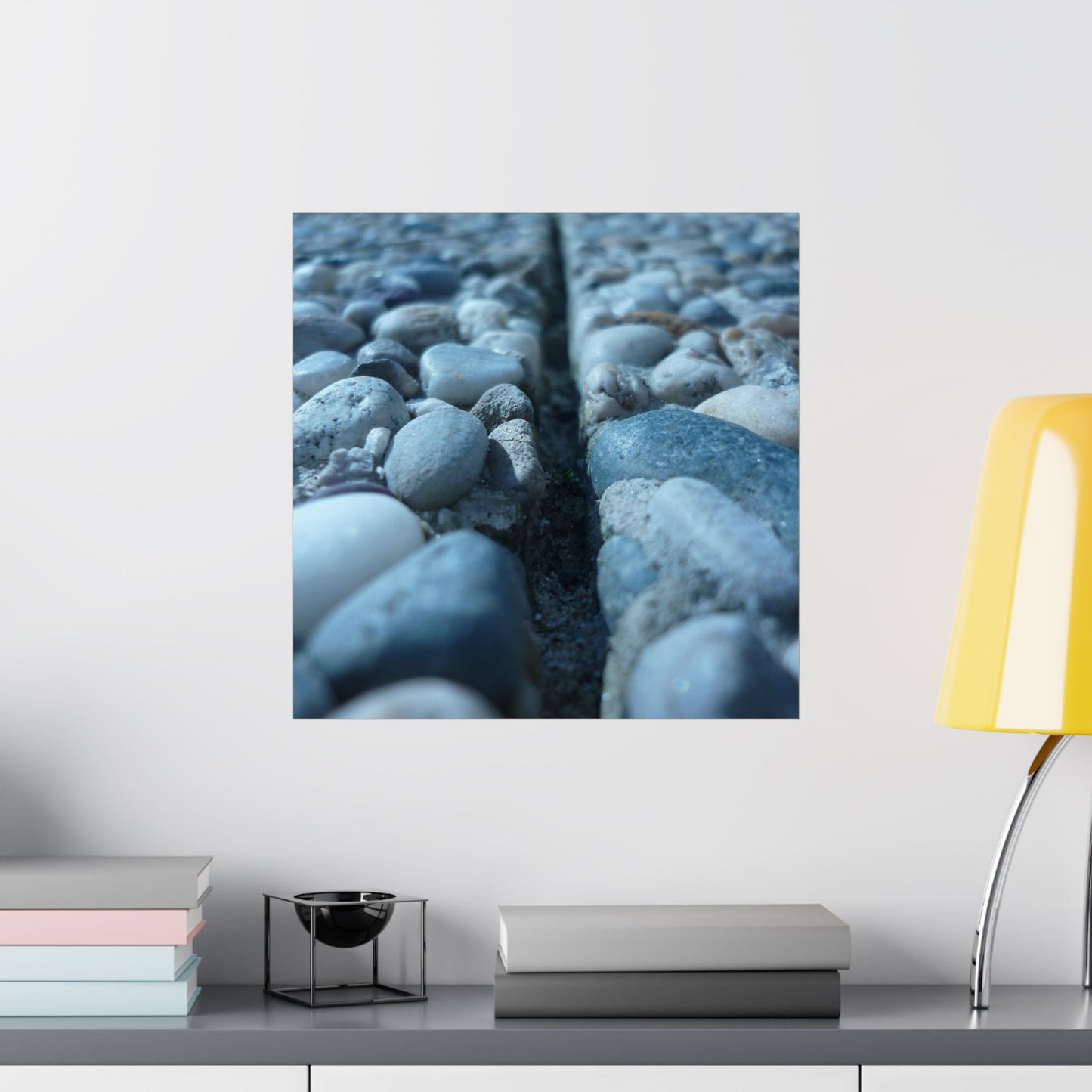 Wall art of pebbles on a white wall with books and a lamp below.